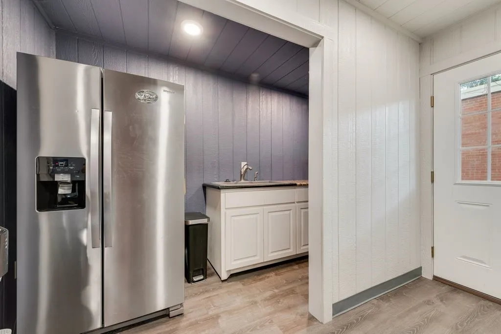 Stainless steel side-by-side refrigerator, wood-finish flooring, recessed lighting, white paneled wall, and white cabinetry with a sink