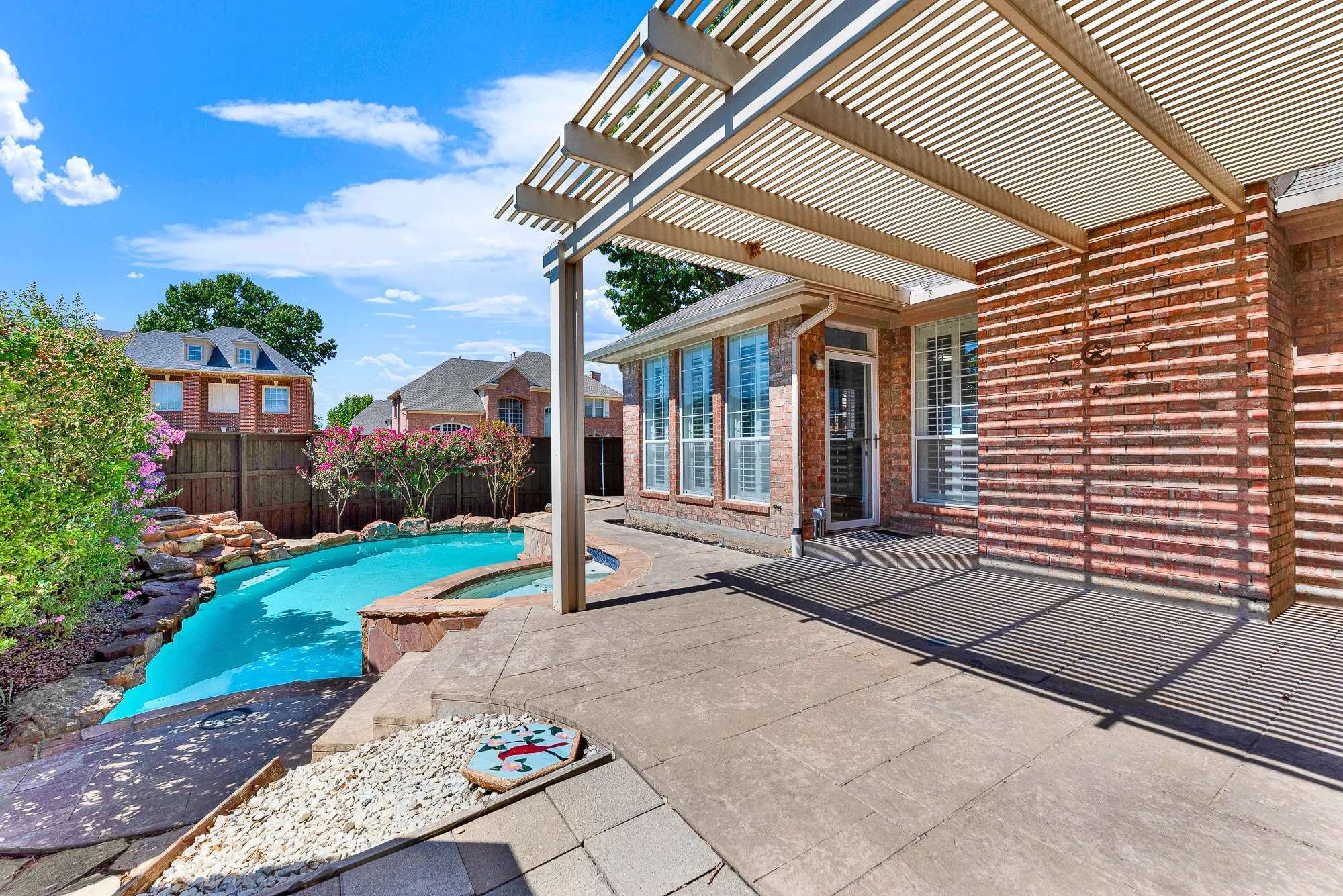 The shaded patio lounge steps down directly toward a pristine back pool setup. Transition easily from lounging under the pergola to taking a refreshing swim.