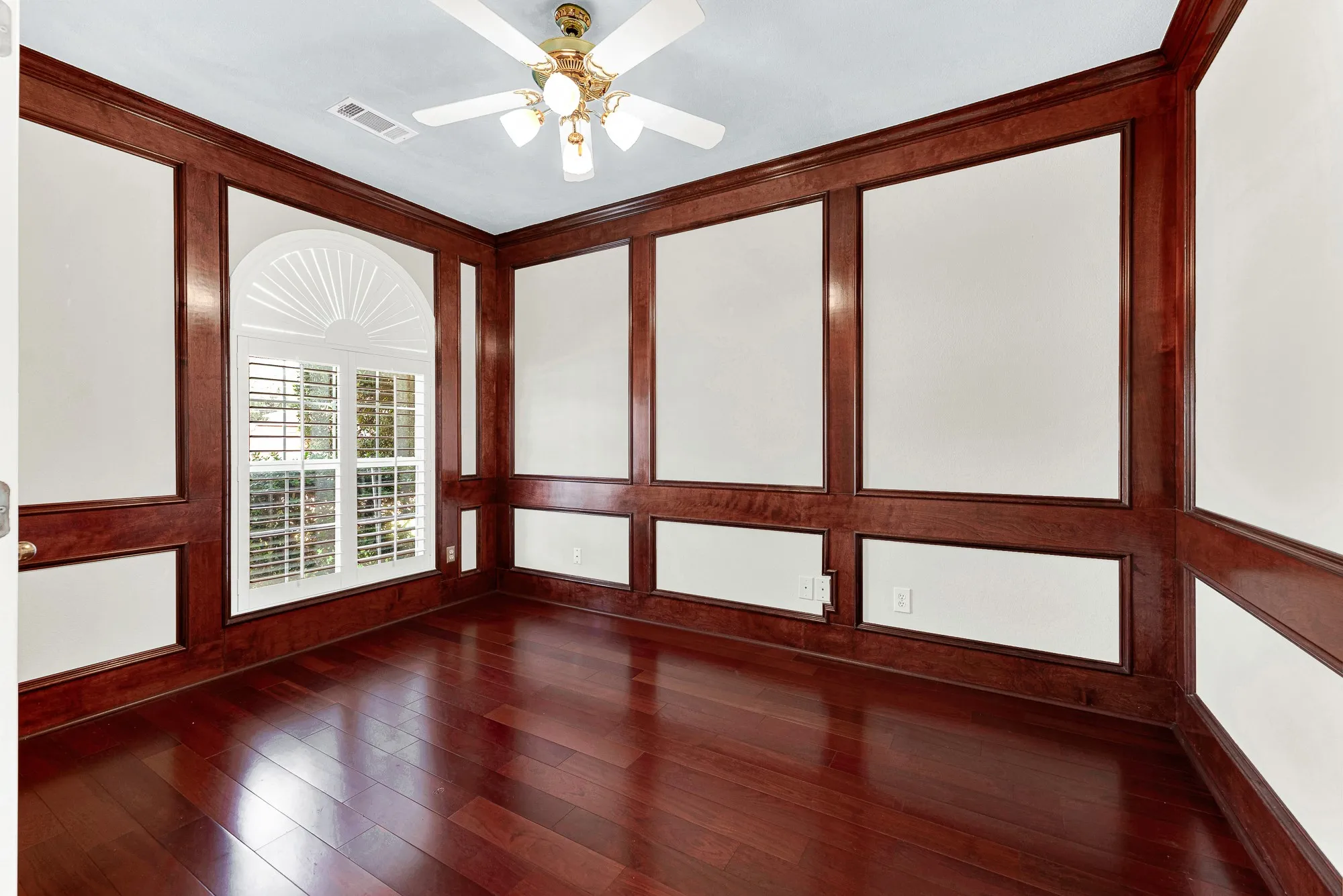 Rich wood millwork frames an arched sunburst window that pours sunlight across deep hardwood planks. Settle in with a notebook and steaming espresso to tackle your morning tasks in peace.