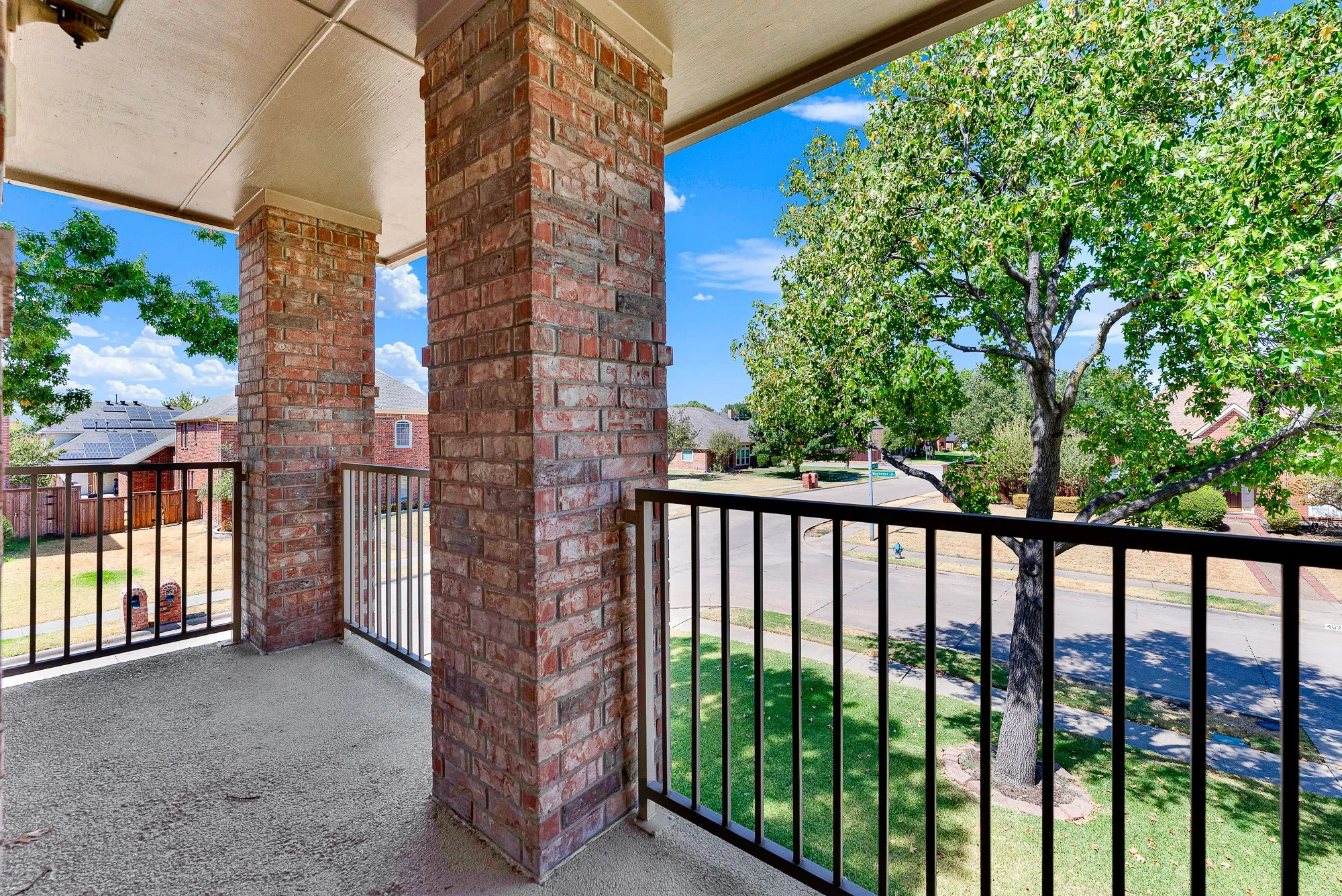 The covered second-floor balcony offers a private outdoor retreat framed by sturdy brick pillars and railing, overlooking the tree-lined neighborhood and front lawn. Step outside to sip your morning coffee while enjoying elevated neighborhood views.