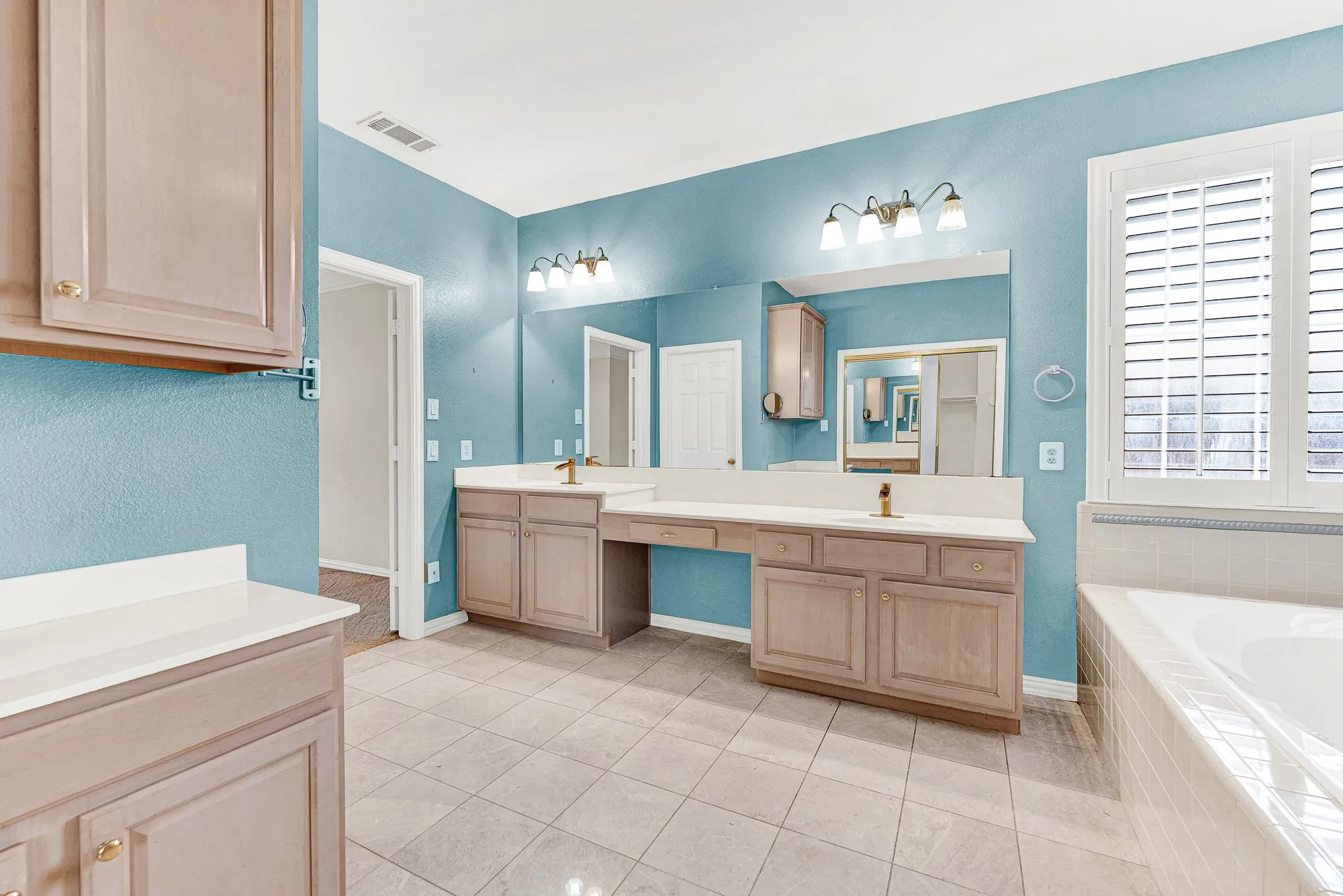 An expansive dual-sink vanity features a built-in makeup station beneath bright vanity lights. Enjoy a smooth, unhurried morning routine side-by-side