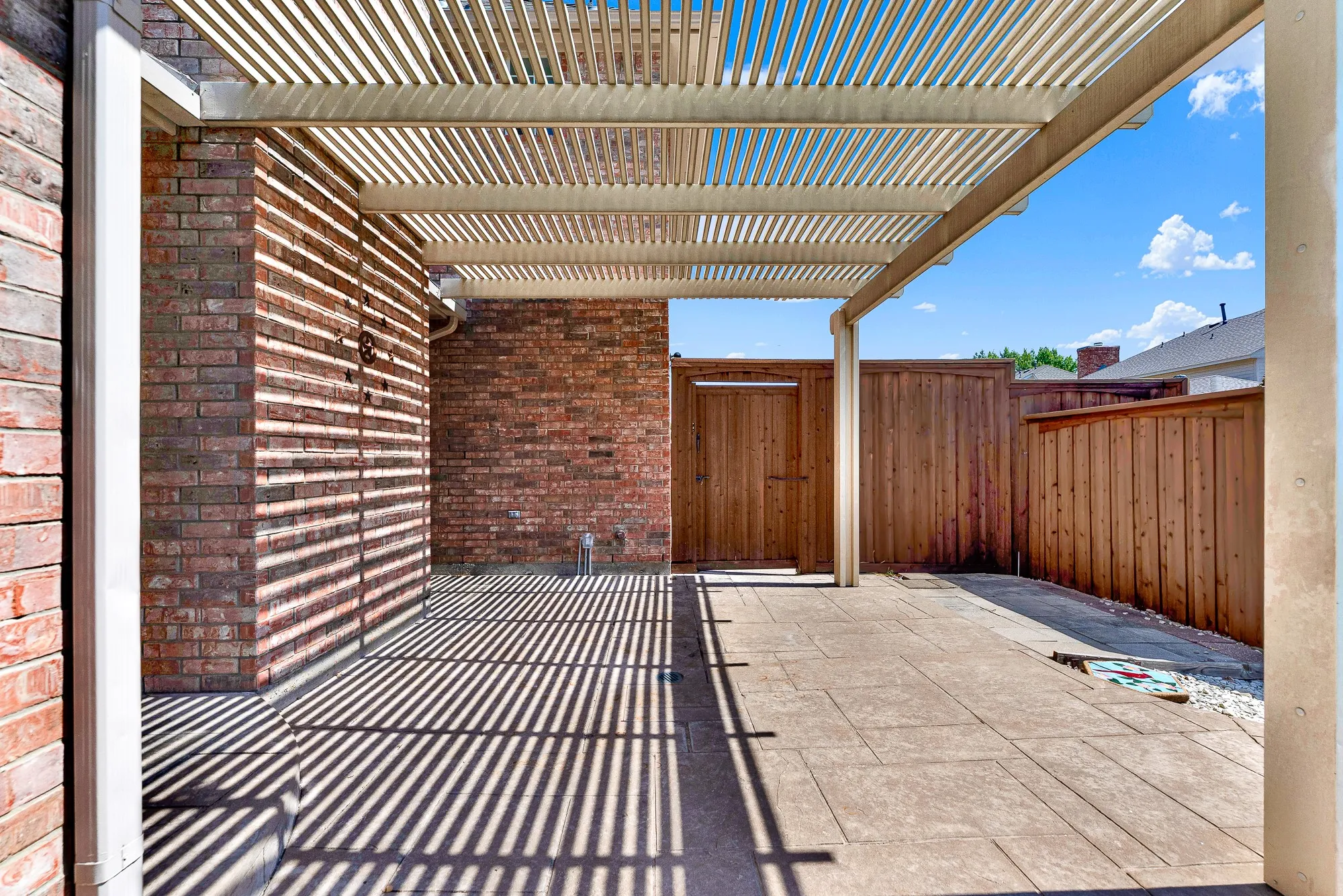 A covered pergola extends over the paved patio area, offering shaded seating surrounded by private wood fencing. Perfect for grilling out or dining alfresco on warm summer afternoons.