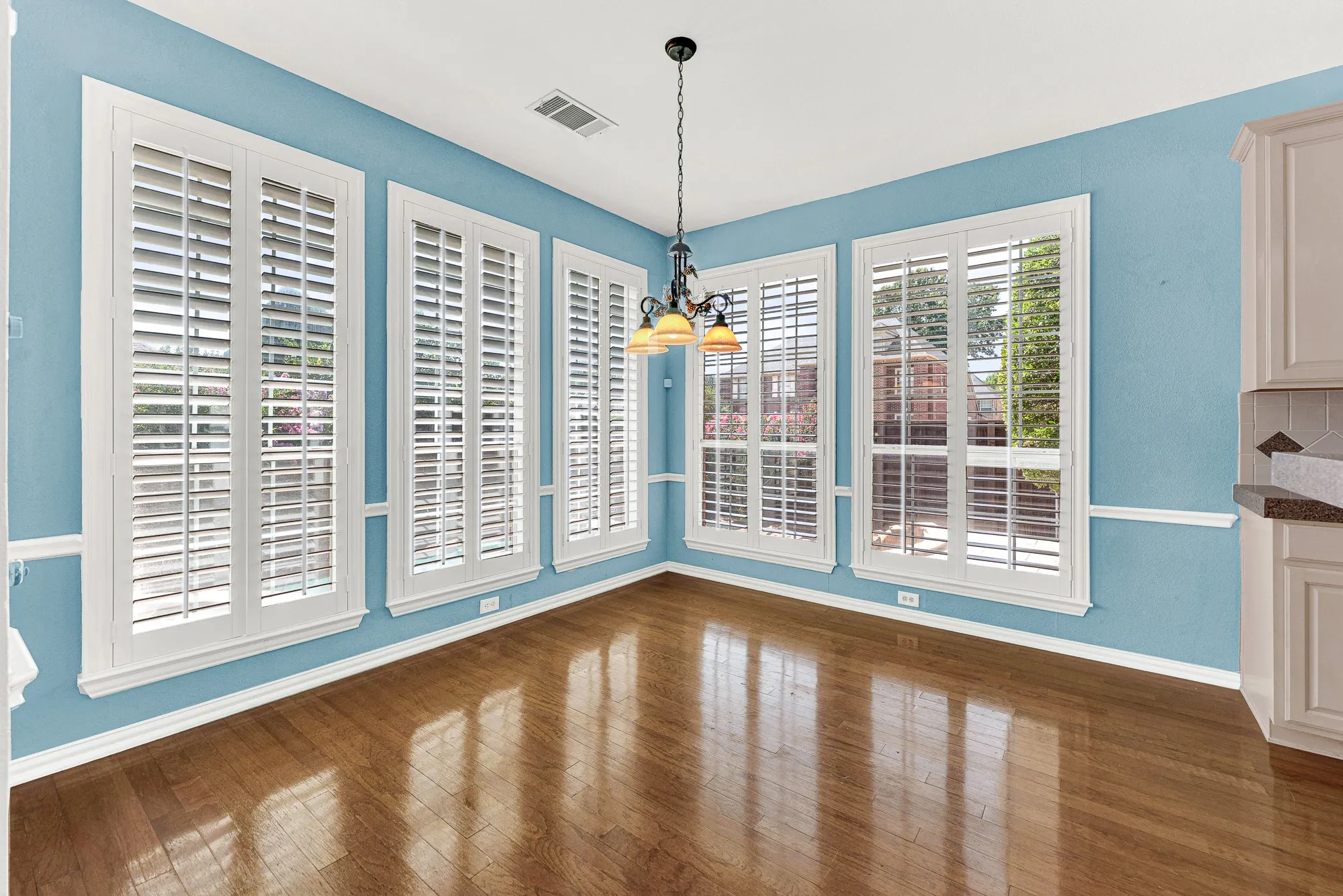 Tall plantation shutters wrap this sunlit corner room beneath an elegant wrought-iron fixture. Sip warm tea while watching the backyard garden wake up in the morning sun.