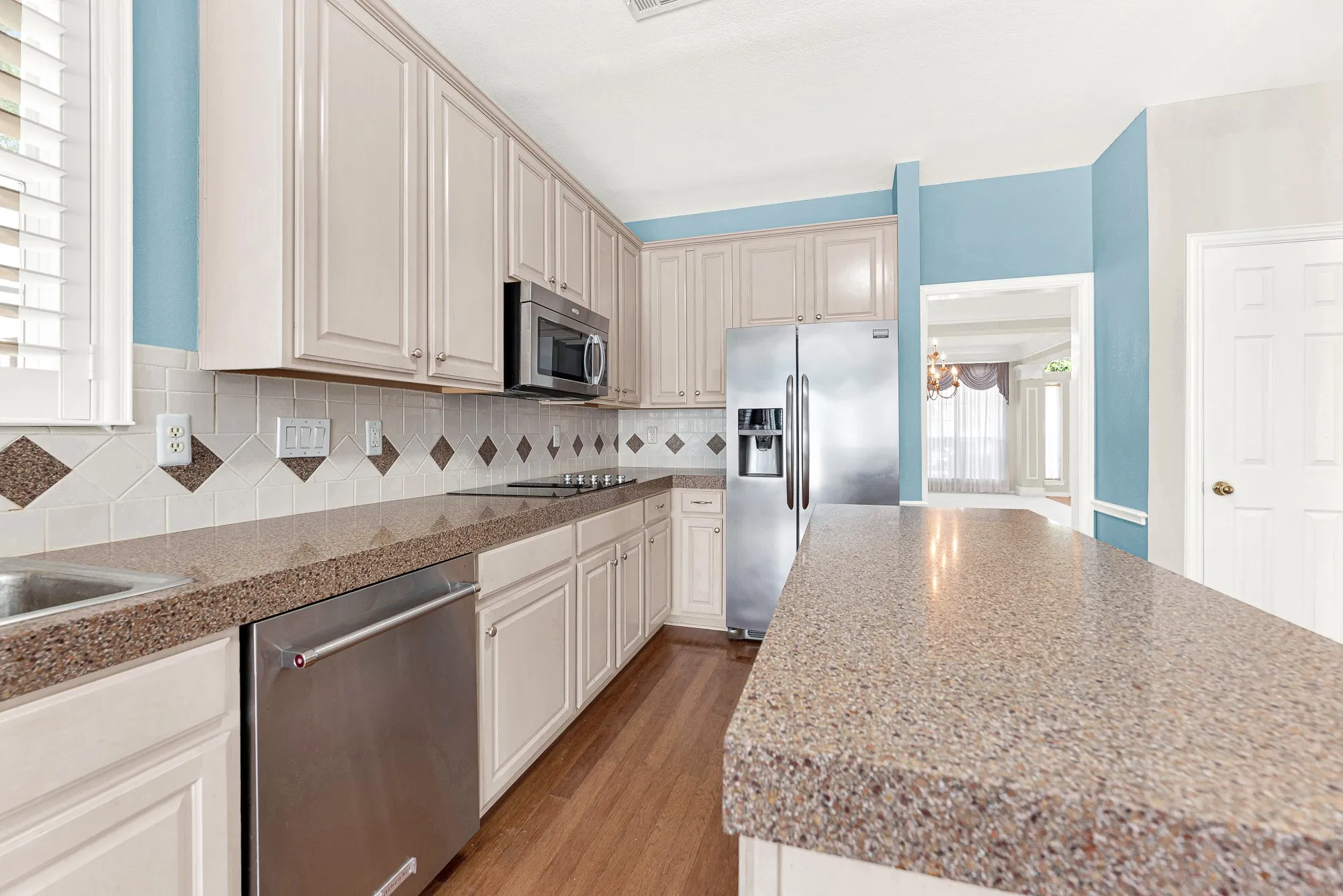 Expansive speckled countertops extend alongside stainless appliances to offer generous workspace. Perfect for spreading out dough to bake morning pastries with family.