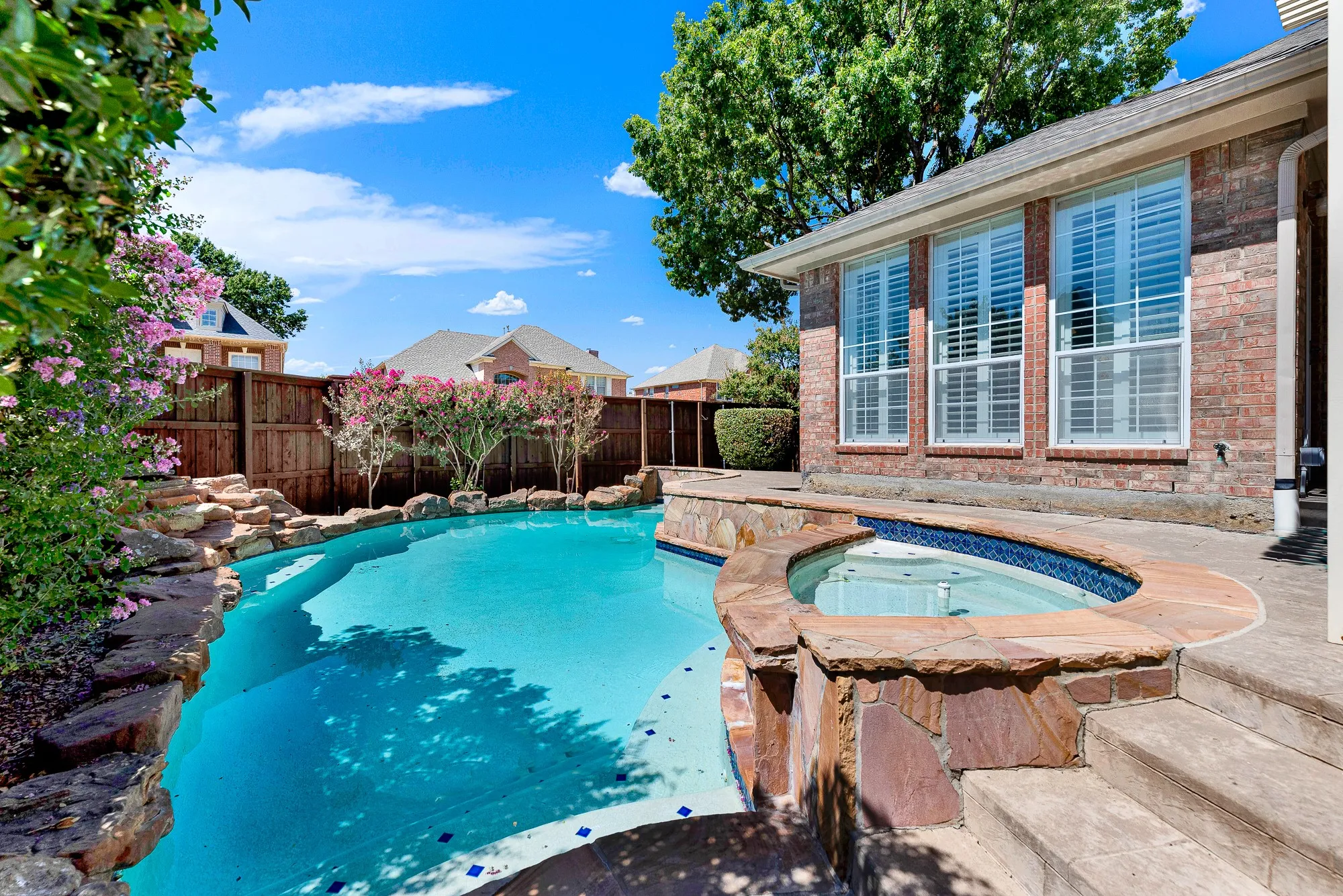 A sparkling in-ground pool and integrated raised spa are surrounded by natural stone coping and lush greenery. Unwind in the bubbling hot tub after a busy workday