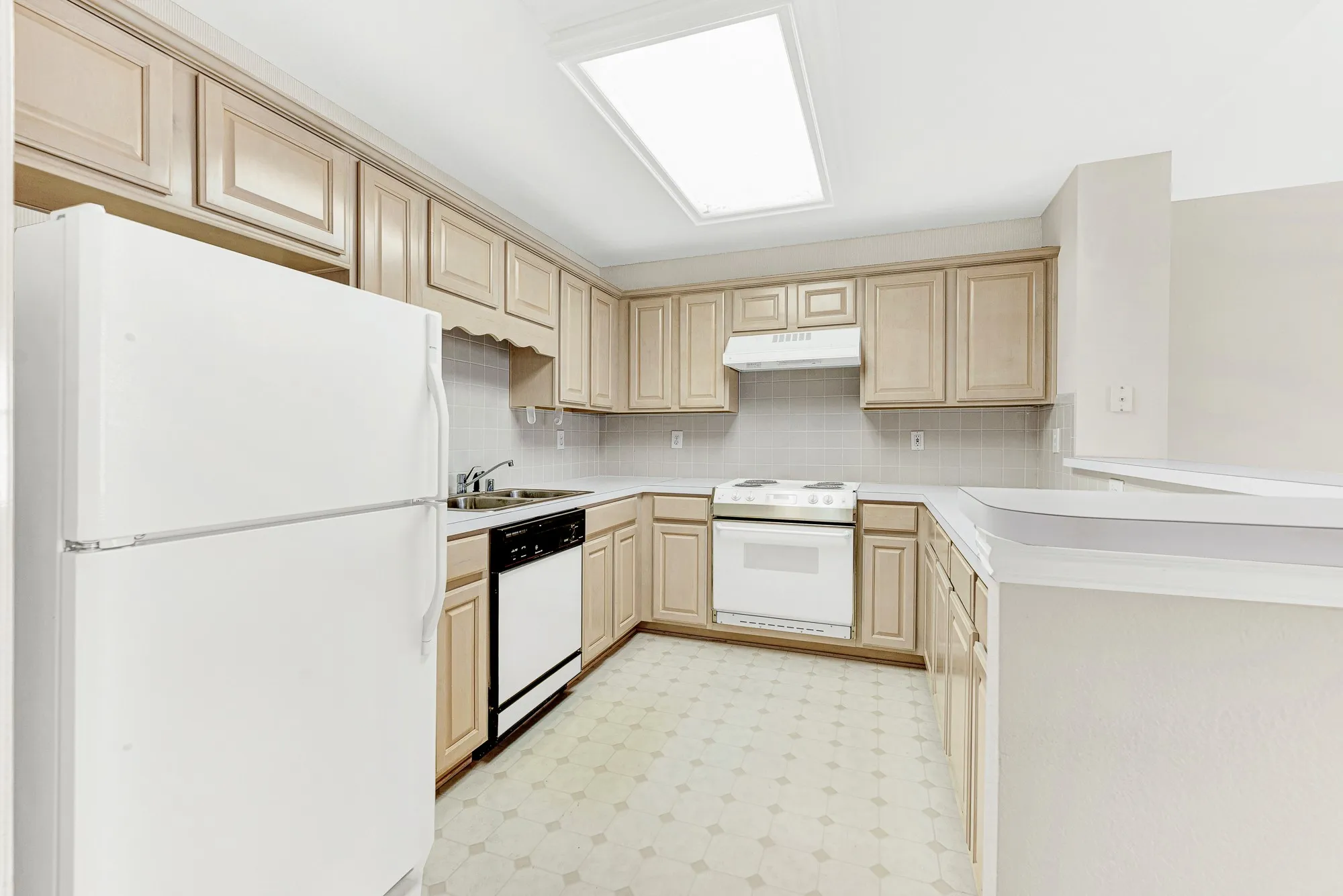 A fully equipped kitchen features full-sized appliances, light cabinetry, and an overhead skylight. Perfect for preparing independent daily meals or late-night snacks.