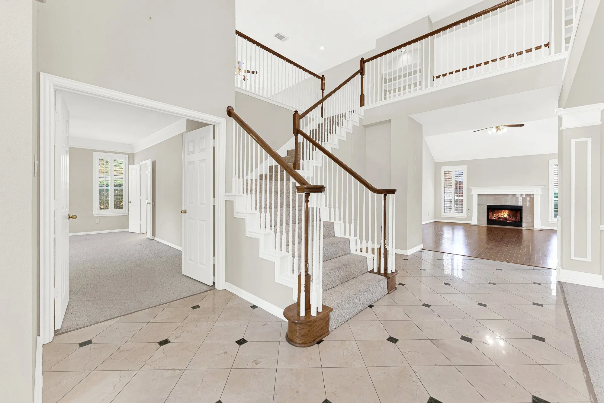 A grand two-story entry foyer features polished tile floors, classic wood banisters, and direct views into adjacent living spaces. Welcome guests into an impressive, light-filled greeting space that sets a welcoming tone