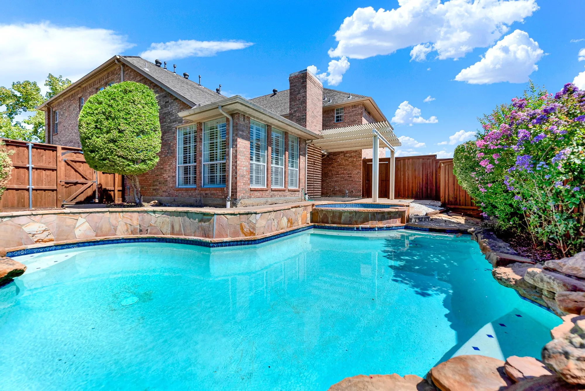 Bright blue water reflects crisp skies beside vibrant flowering crepe myrtles along the fence line. Host unforgettable weekend pool parties for family and friends all season long.