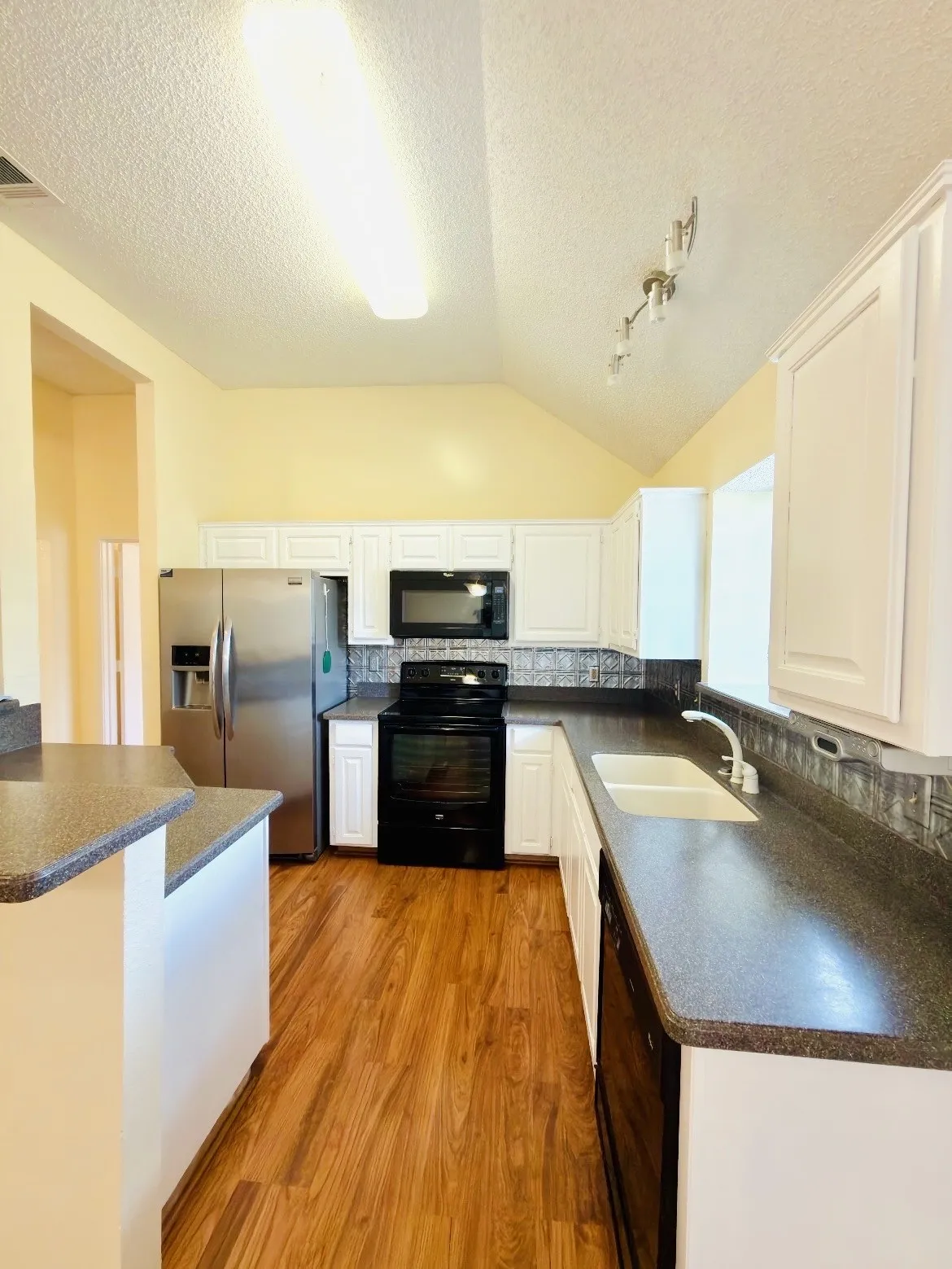 Vaulted ceiling kitchen featuring wood-finish flooring, white cabinetry, dark countertops, and stainless-steel appliances