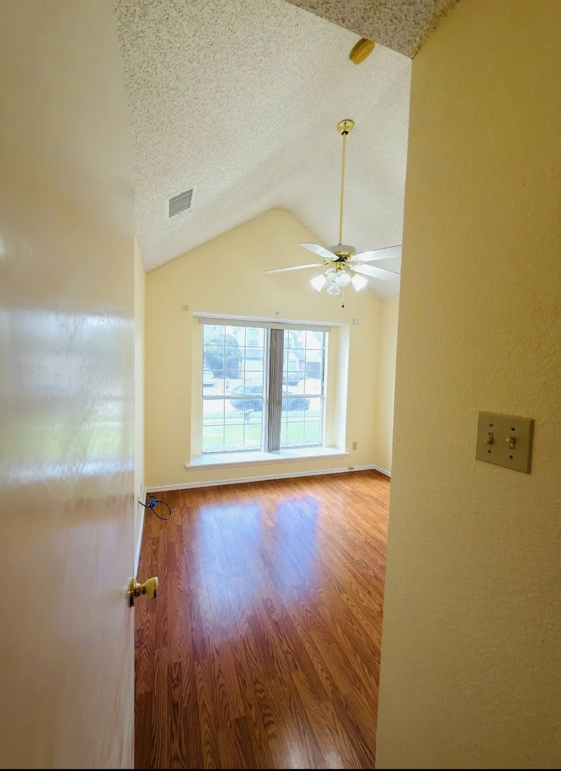 Vaulted ceiling, wood-finish flooring, ceiling fan with integrated lighting, and a large window