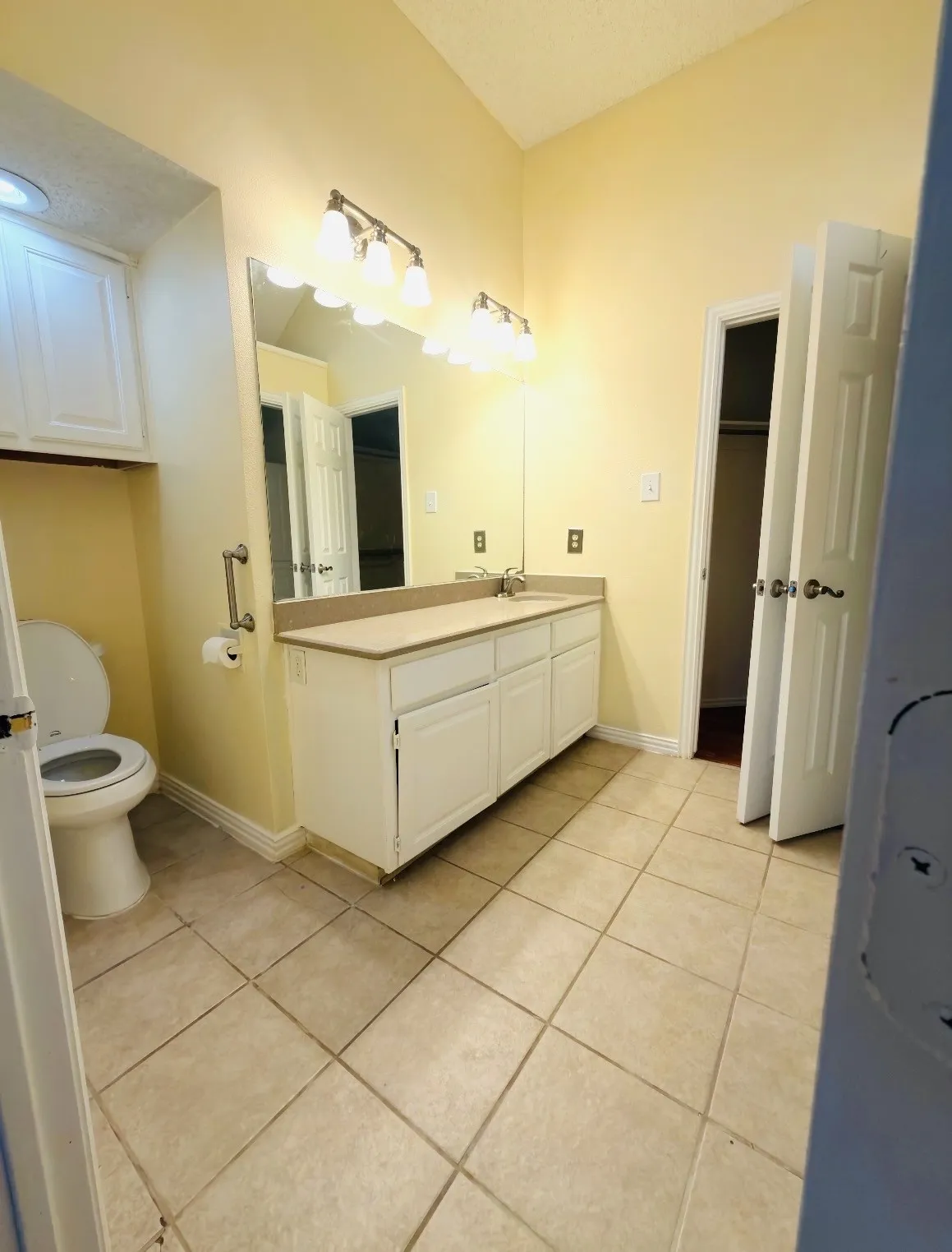 Bathroom with vaulted ceiling, large vanity mirror, built-in storage cabinet, and tile flooring