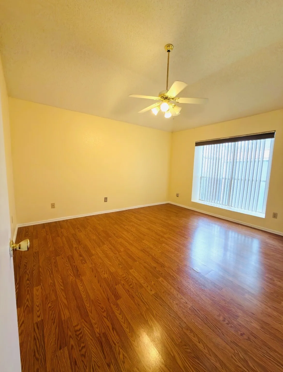 Wood-finish flooring, ceiling fan with integrated lighting, and window with vertical blinds