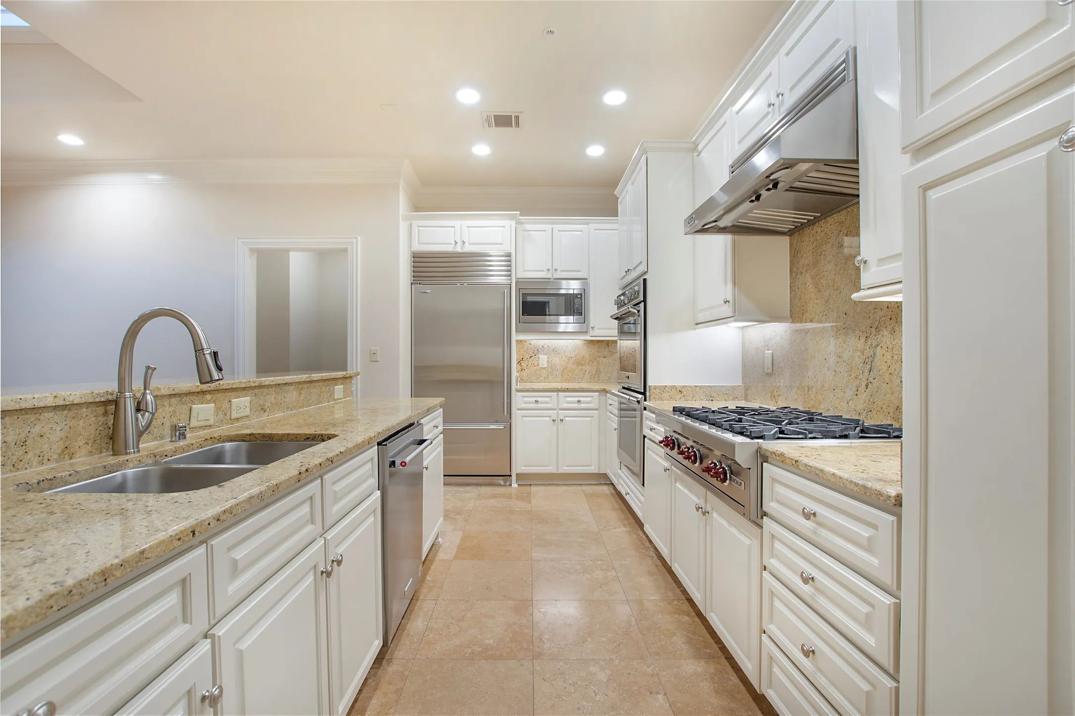 Kitchen with tasteful backsplash, light stone countertops, sink, white cabinetry, and built in appliances