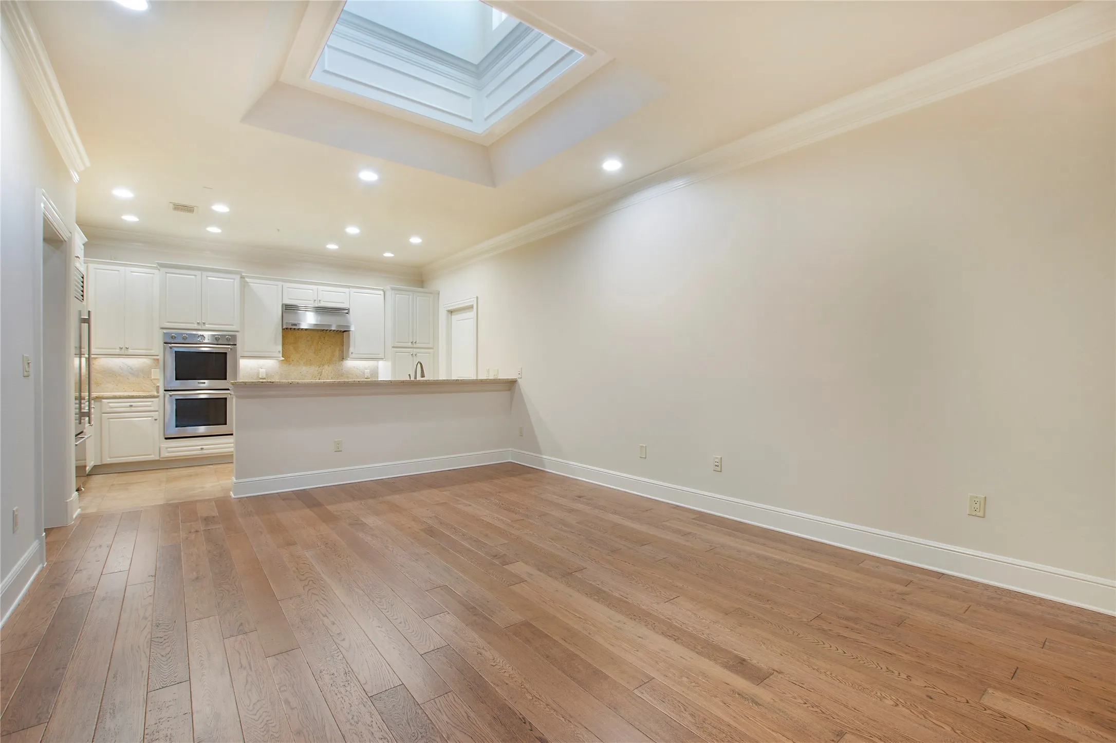 Unfurnished living room with light hardwood / wood-style flooring, a tray ceiling, ornamental molding, and a skylight