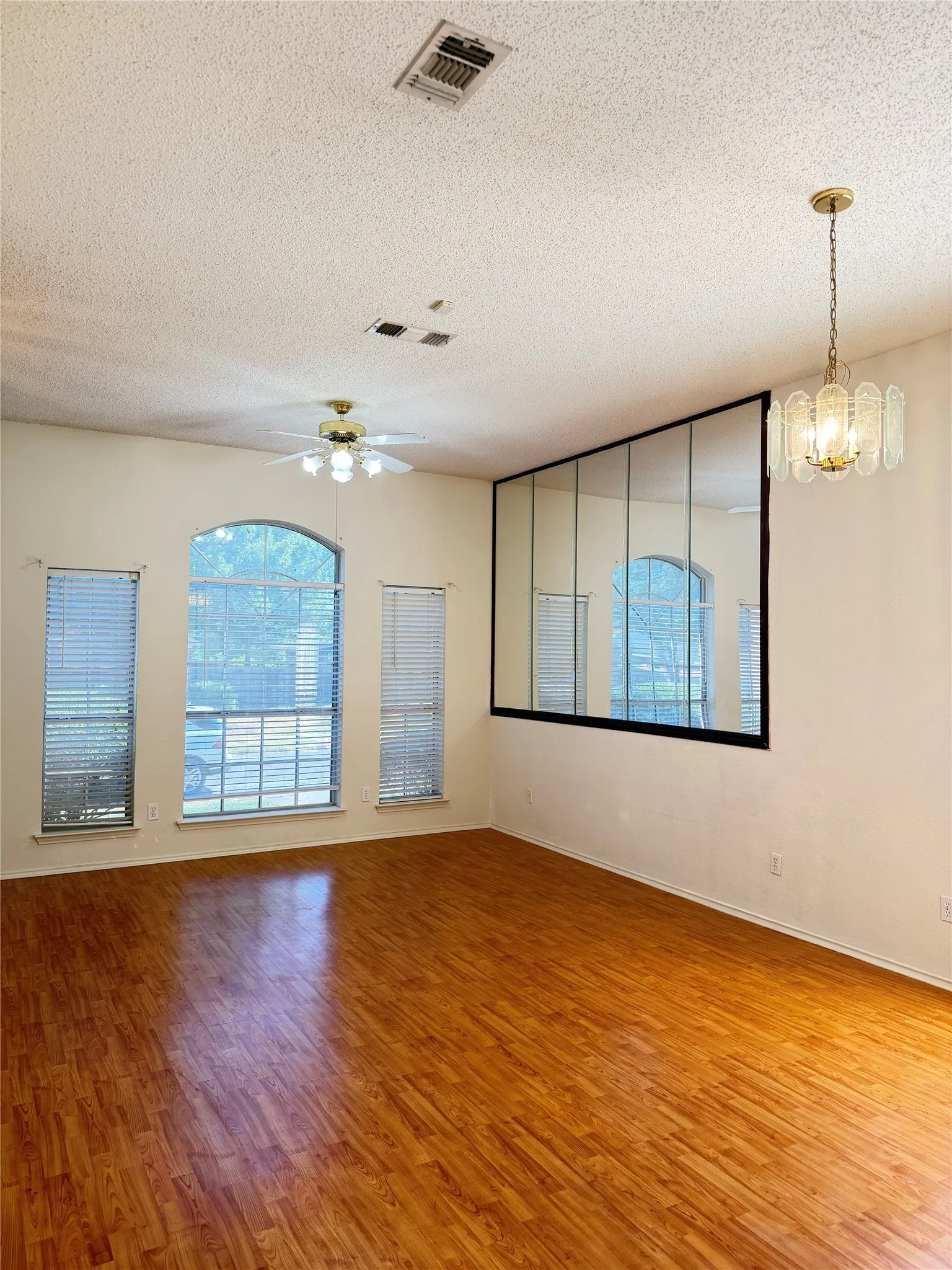 Wood-finish flooring throughout, multiple windows with blinds, a ceiling fan, and a decorative pendant light fixture