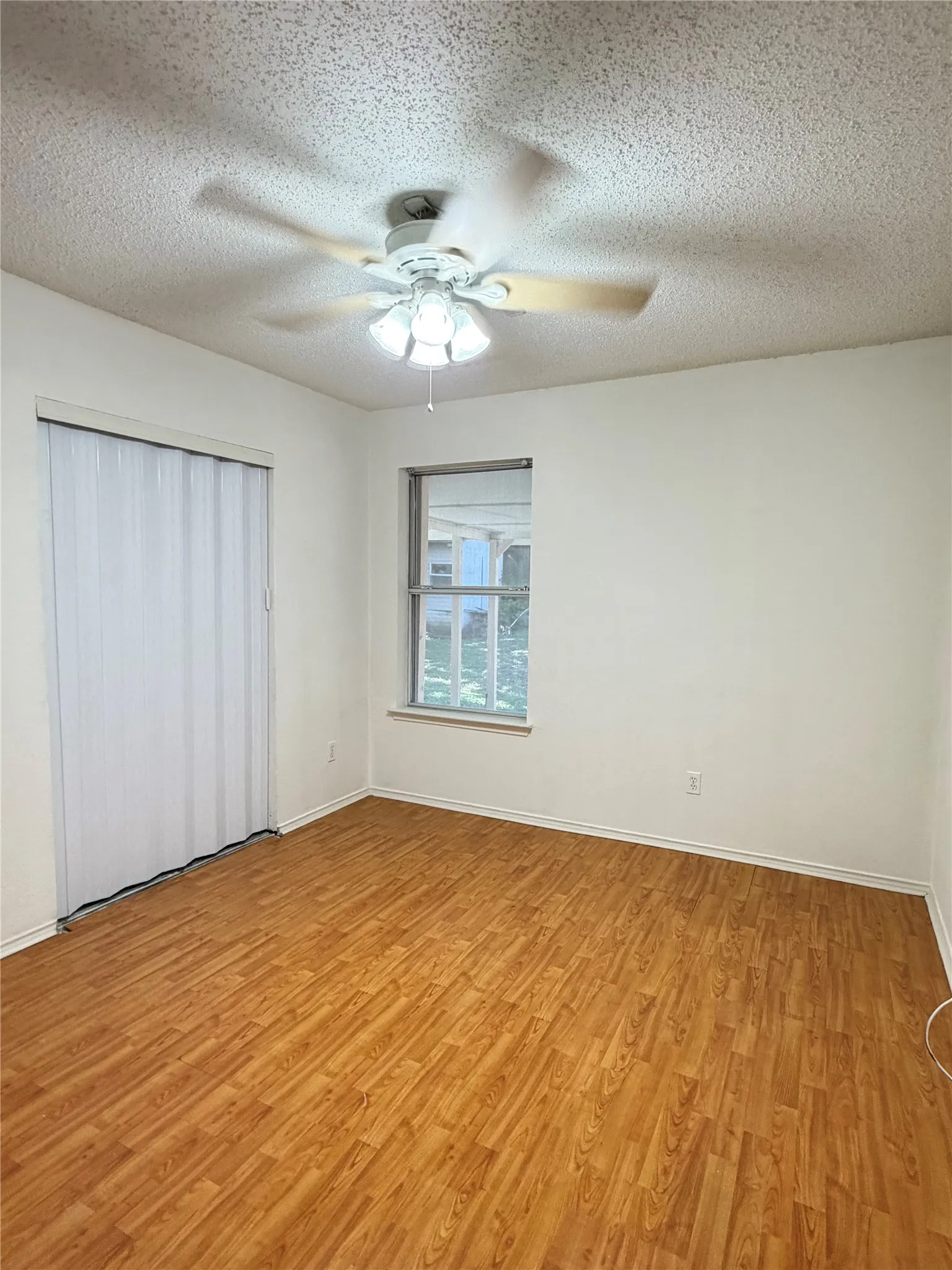 Wood-finish flooring, ceiling fan with integrated lighting, and a window providing natural light