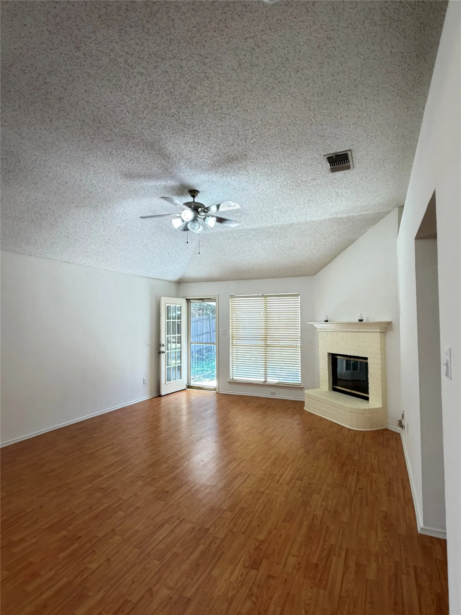 Spacious living area featuring wood-finish flooring, a corner fireplace with a hearth, and ample natural light from exterior windows