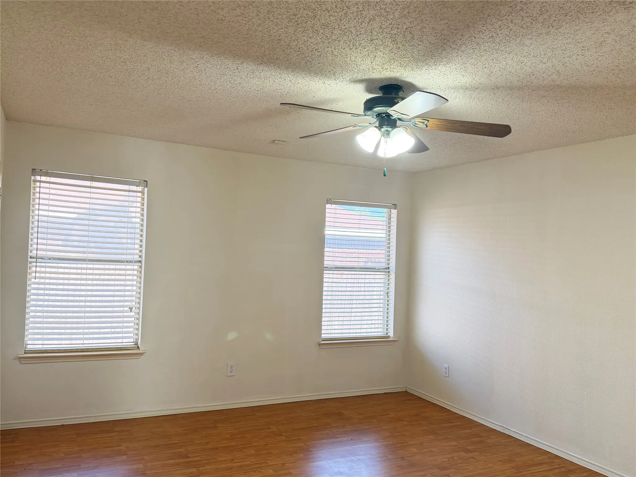 Wood-finish flooring, two windows with blinds, ceiling fan with integrated lighting, and neutral wall tones