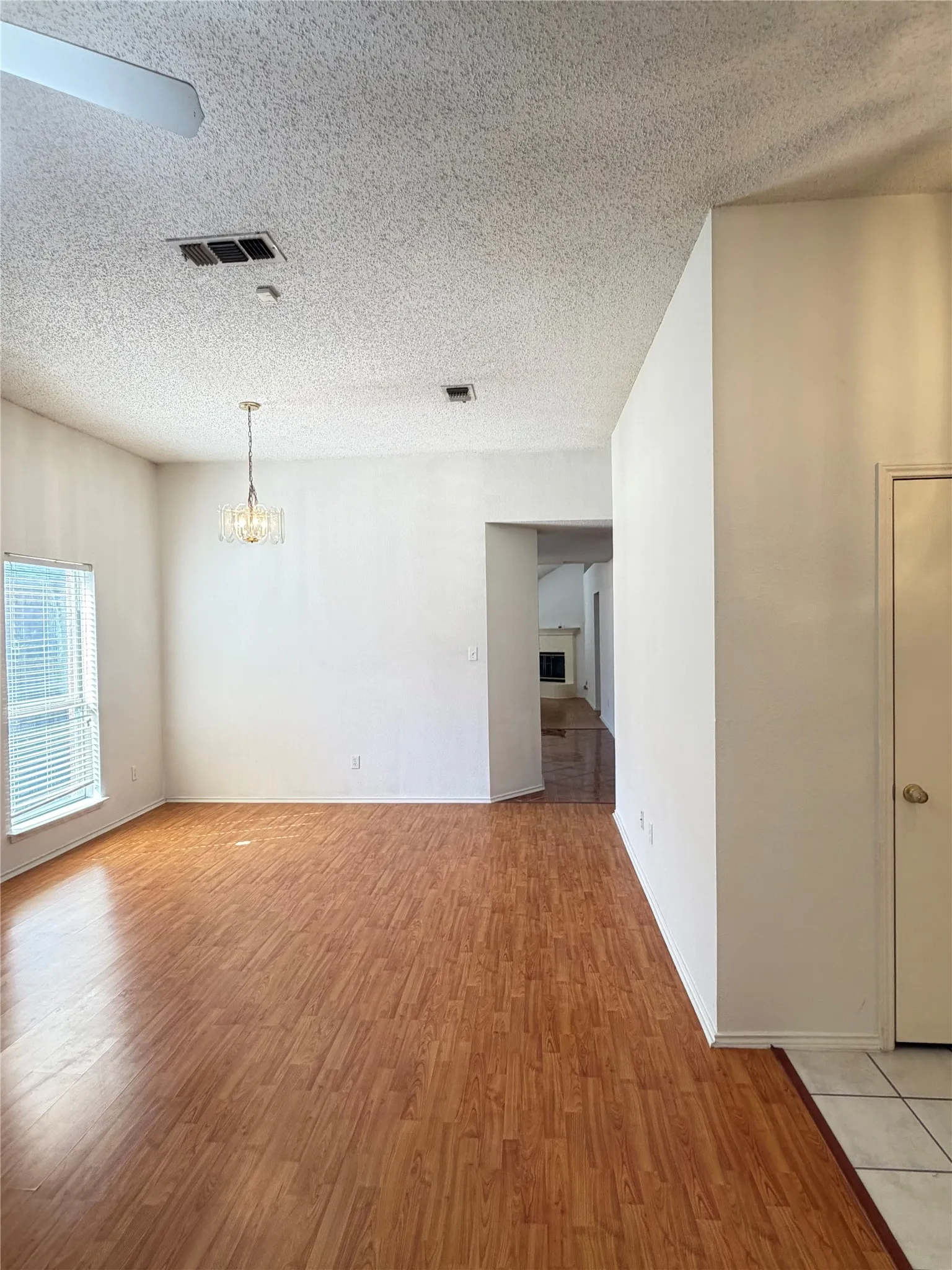Wood-finish flooring, ceiling fan, contemporary chandelier, white walls, and a window with horizontal blinds