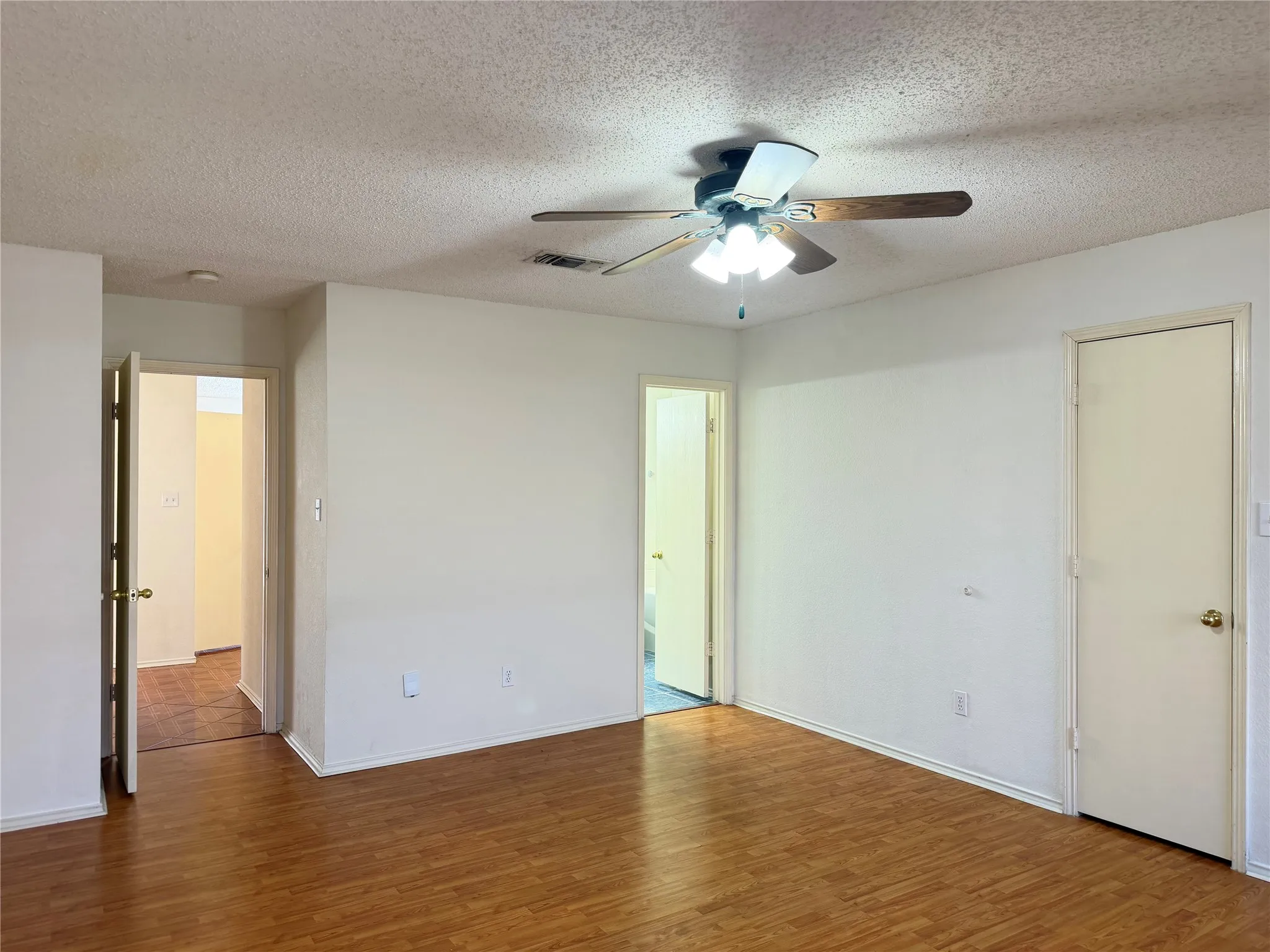 Wood-finish flooring, ceiling fan with integrated lighting, and multiple interior doors