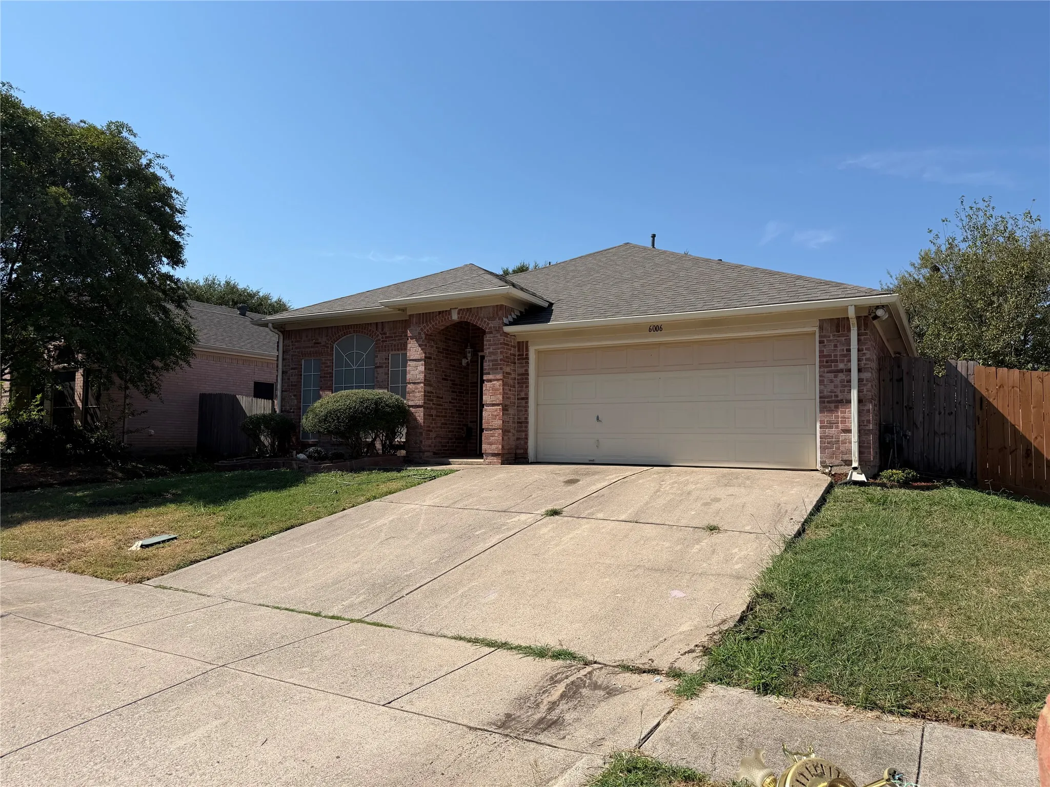 Brick exterior with an attached garage, featuring a concrete driveway and mature landscaping