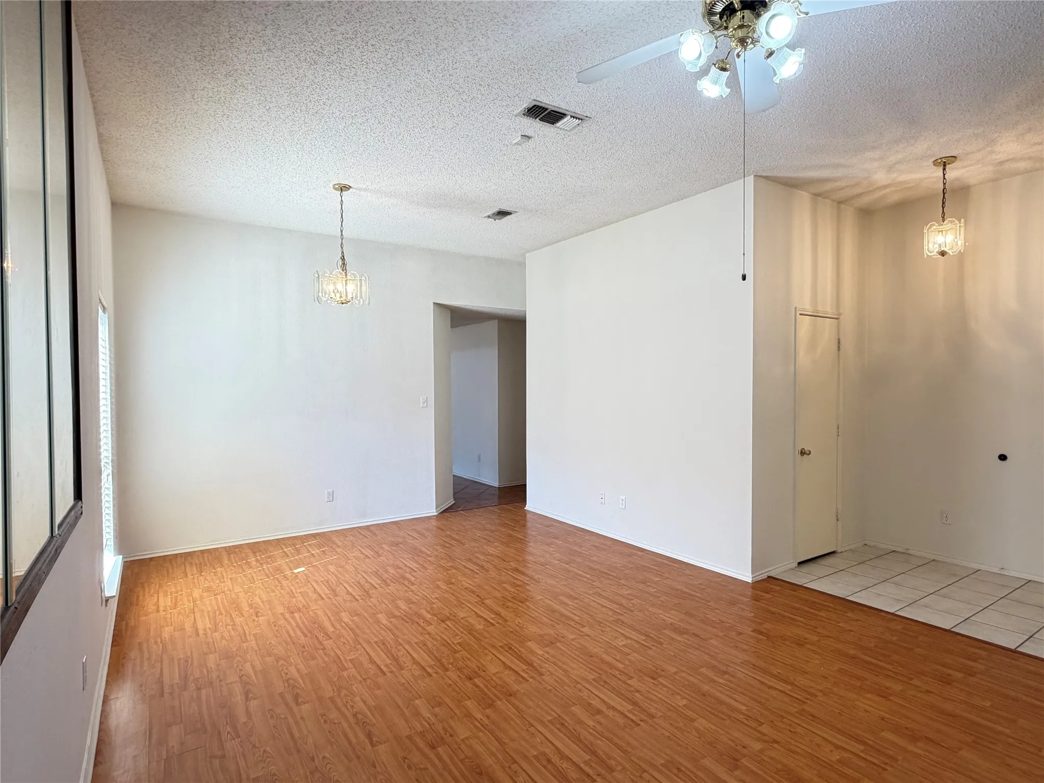 Wood-finish flooring, white walls, vaulted ceiling, dual chandelier lighting, and a ceiling fan