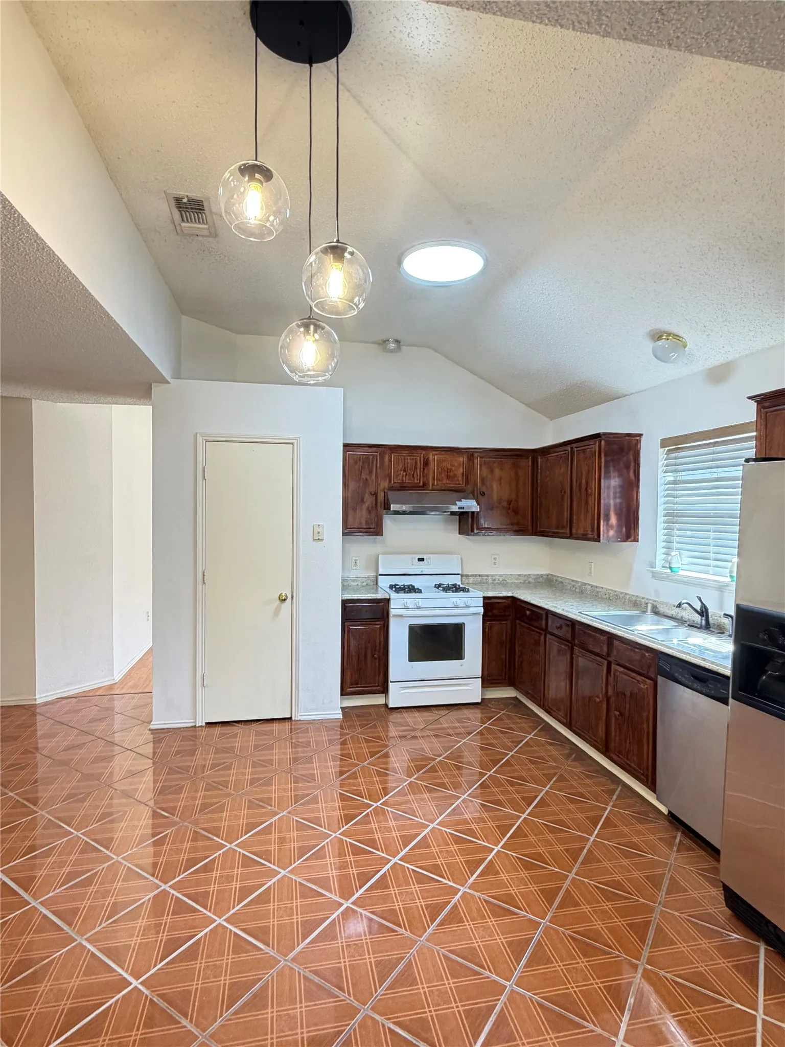 Kitchen featuring a vaulted ceiling, pendant lighting, a built-in oven range, wood-finish cabinetry, and patterned tile flooring