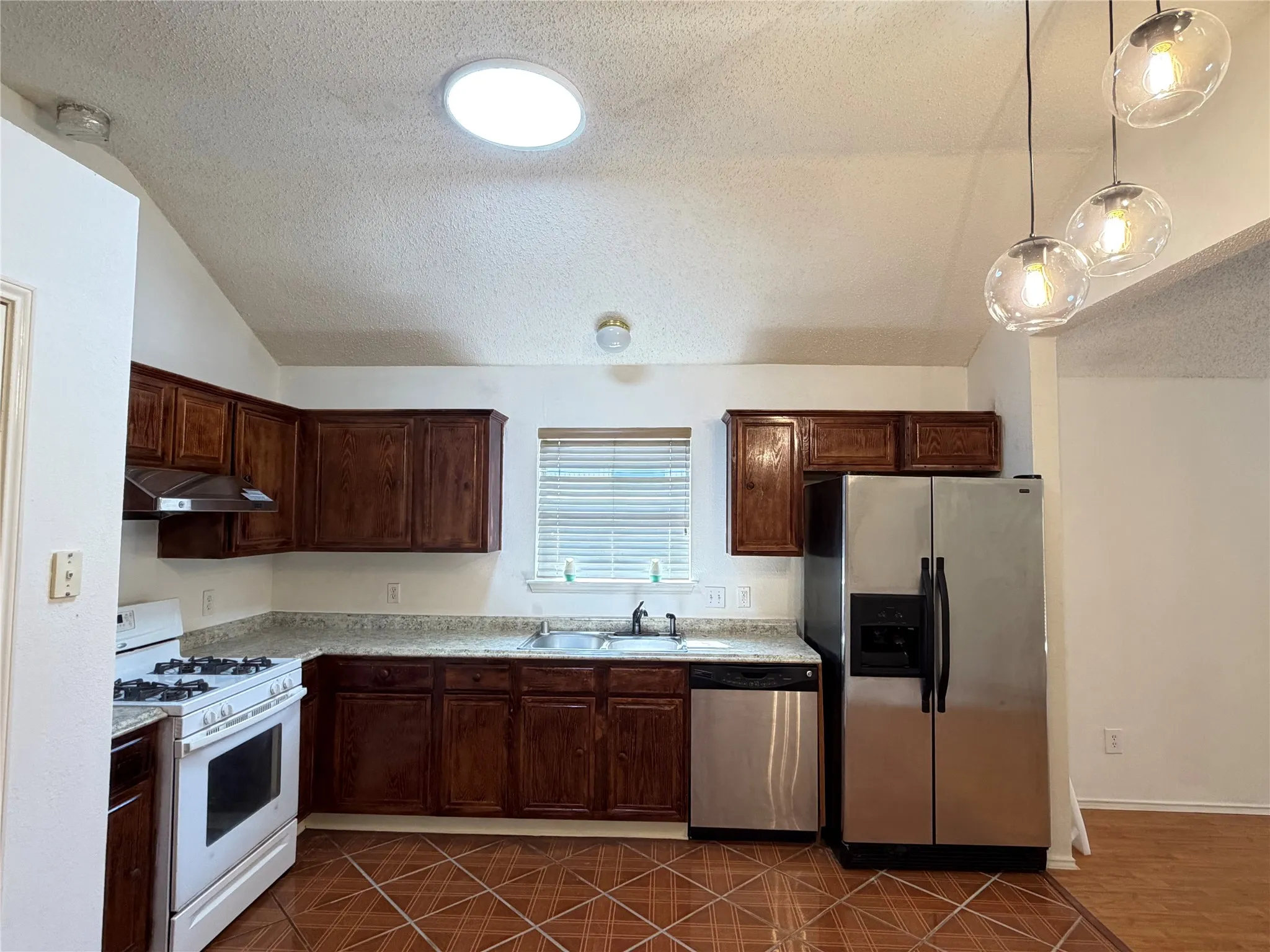 Kitchen featuring vaulted ceilings, a skylight, wood cabinetry, granite-finish countertops, and stainless steel appliances