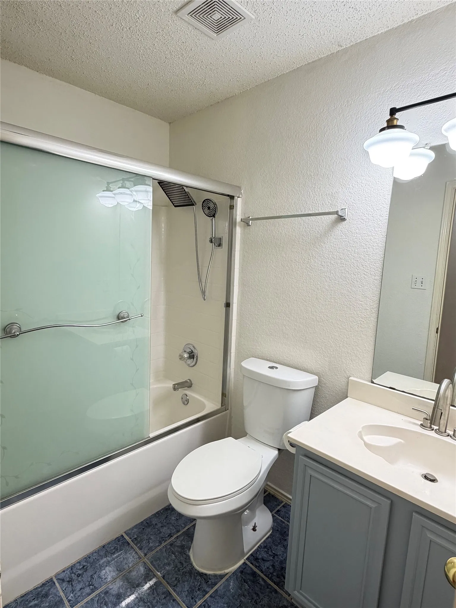 Bathroom featuring a shower-tub combination with sliding glass enclosure, white toilet, vanity with a light-colored countertop, and a wall-mounted light fixture