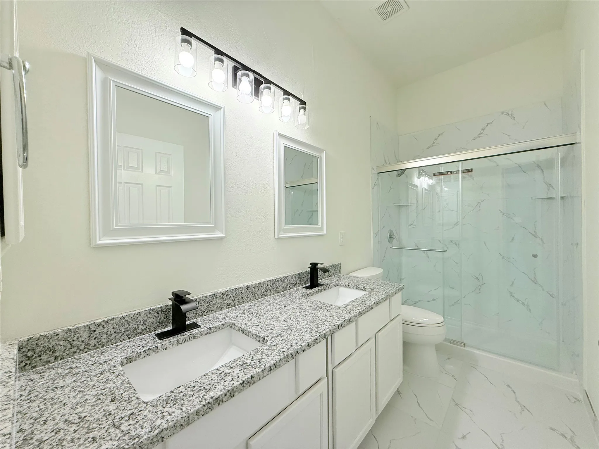 Dual vanity with granite-style countertops, matte black fixtures, and framed mirrors