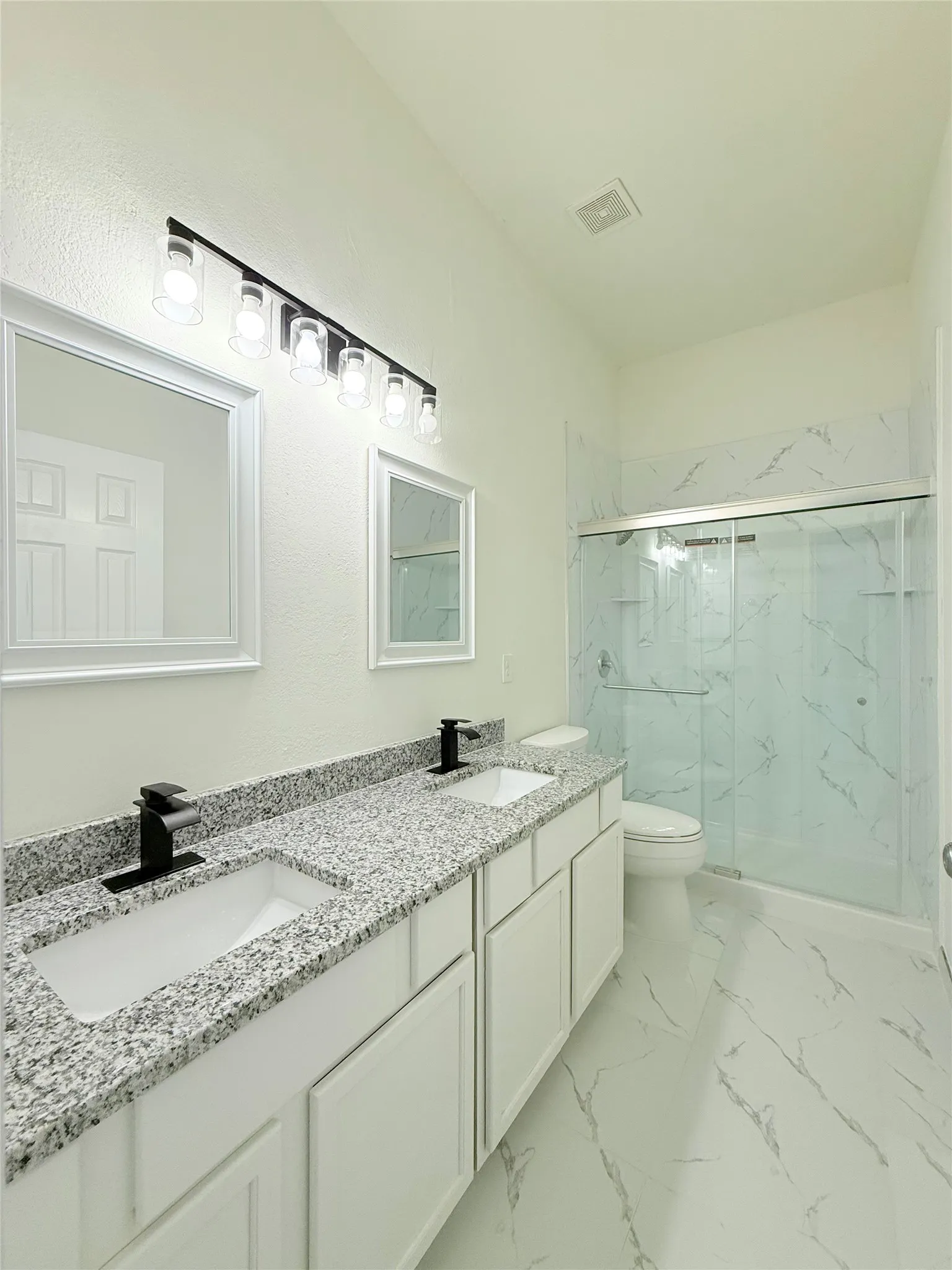 Dual vanity with granite countertops, white cabinetry, and matte black fixtures