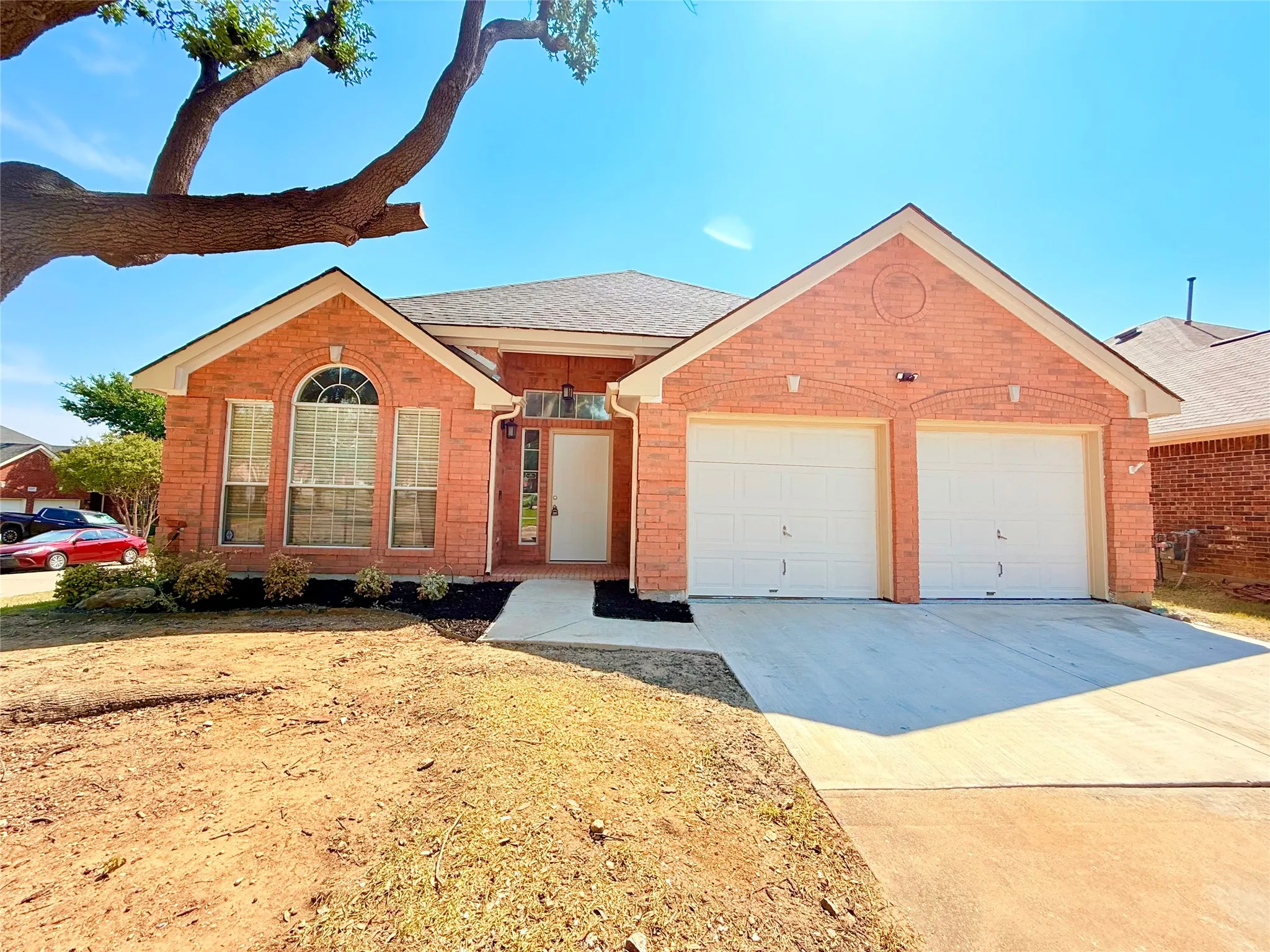 Brick exterior with a gabled roofline, arched front window, concrete driveway, and two garage doors