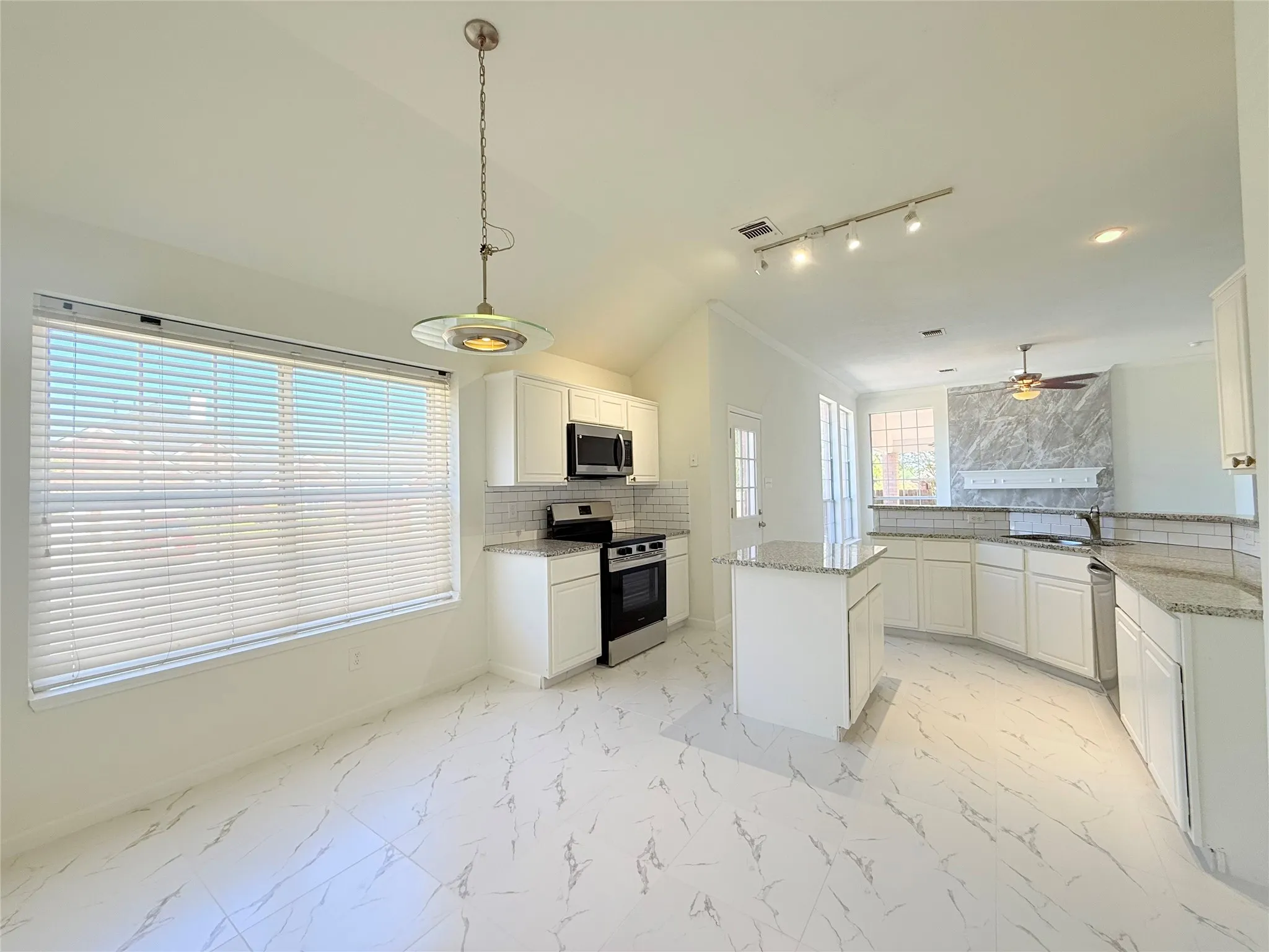 Vaulted ceiling with track lighting, white cabinetry, stainless steel appliances, granite countertops, and patterned tile flooring
