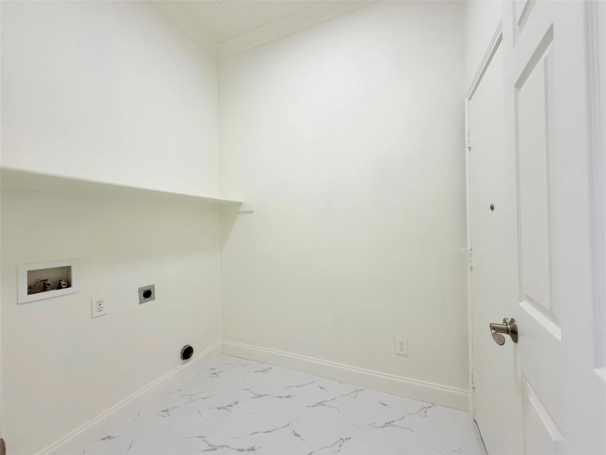 Laundry area featuring white walls, a built-in shelf, and marble-patterned flooring