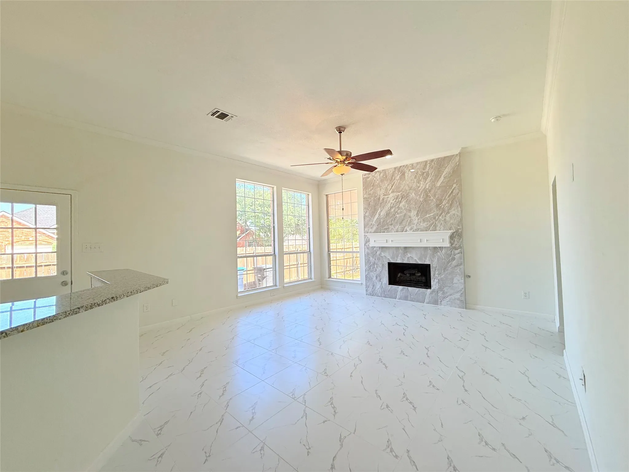 Spacious living area featuring large-format marble-look floor tile, a floor-to-ceiling fireplace with a decorative mantel, and multiple windows