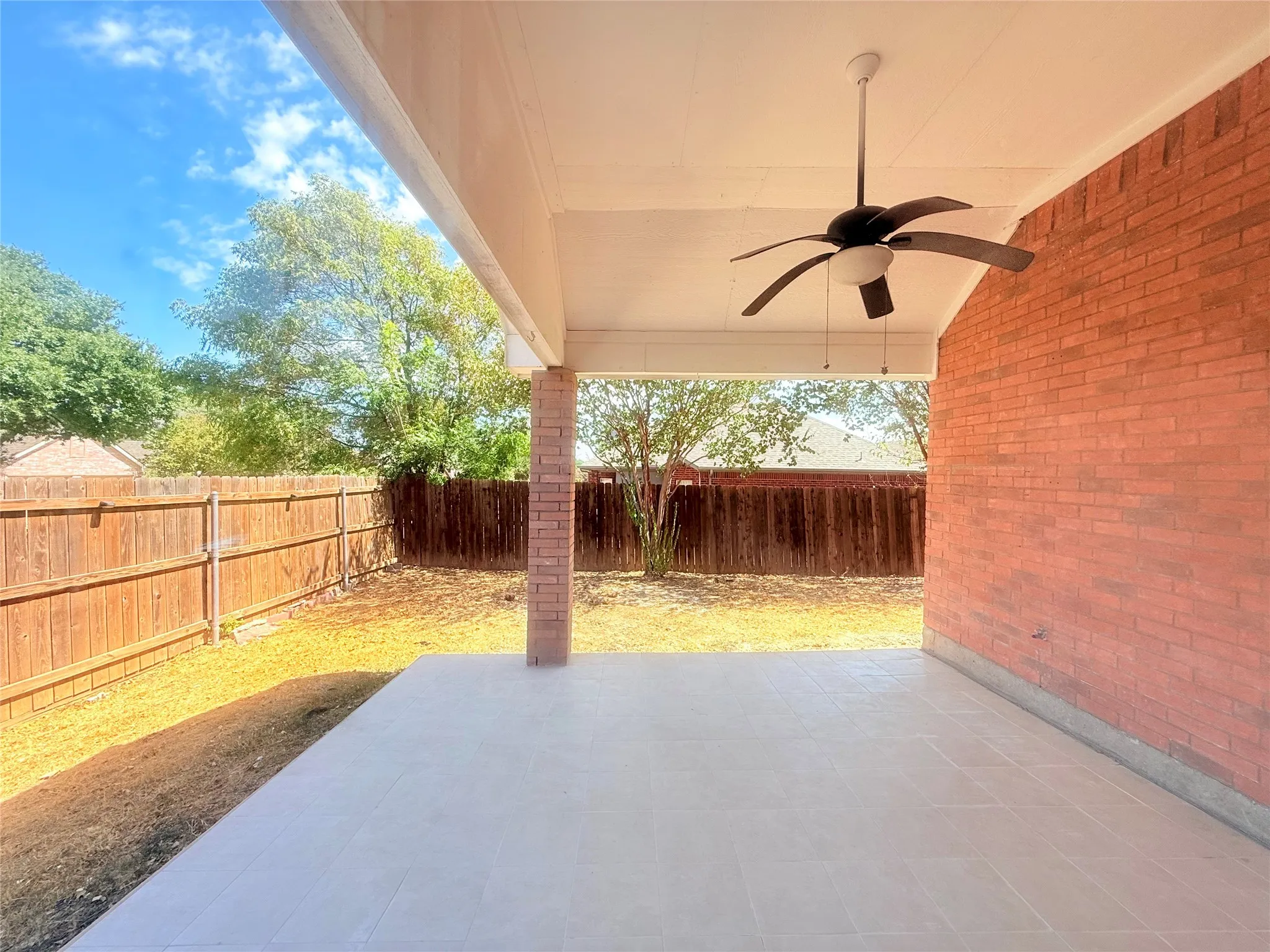 Covered patio featuring a ceiling fan with integrated lighting, brick exterior wall, and tile flooring