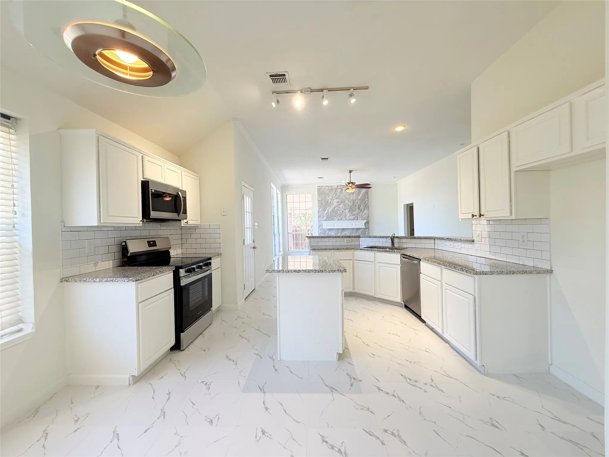 Kitchen featuring white cabinetry, granite countertops, subway tile backsplash, stainless steel appliances, and a central island