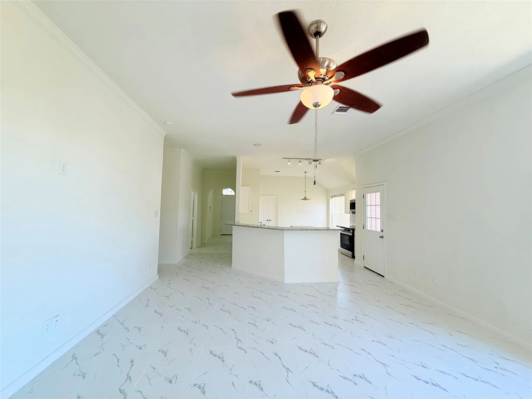 Spacious room with crown molding, ceiling fan, and large format tile flooring