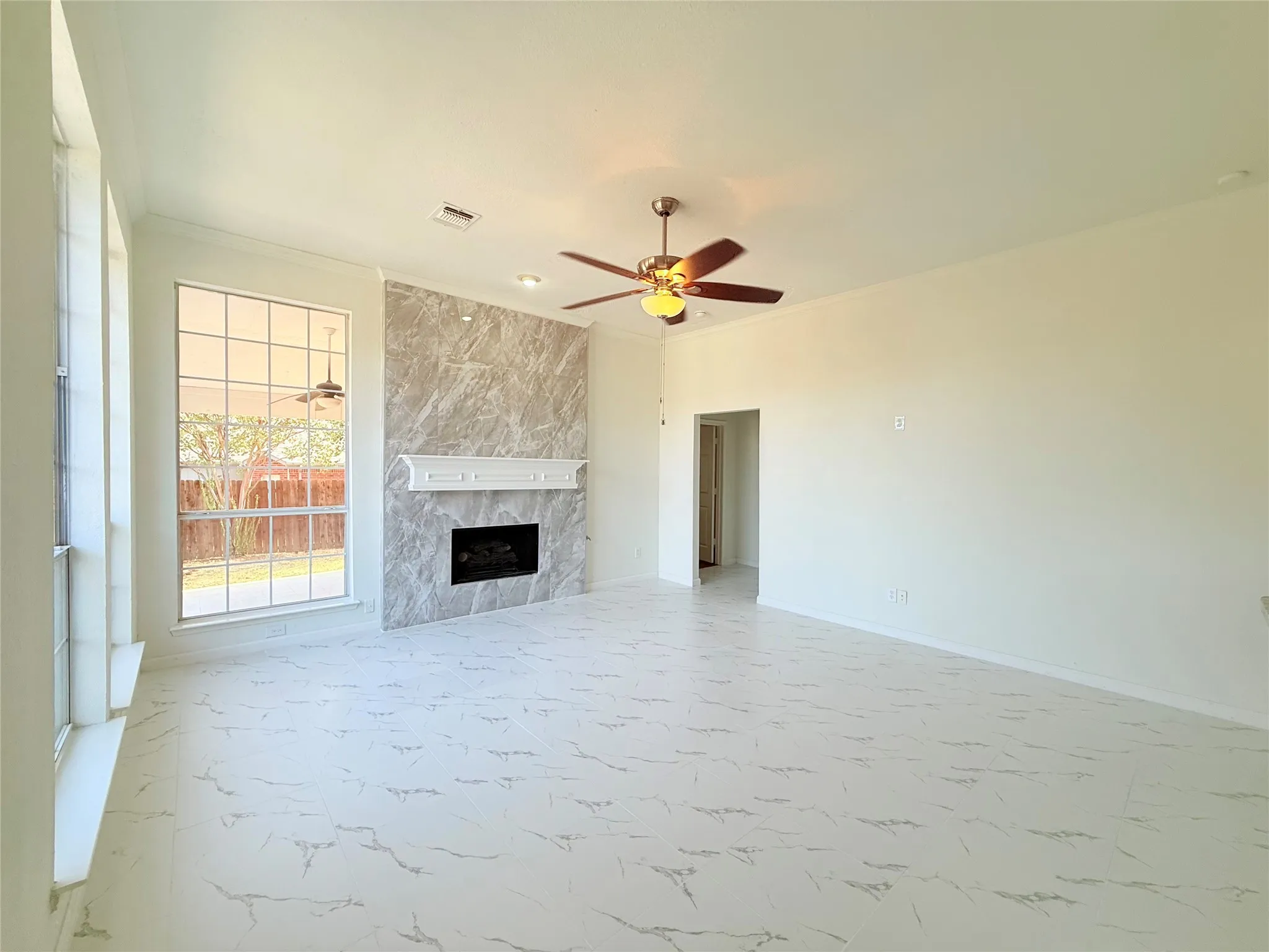 Spacious living area featuring large windows, a ceiling fan, and a fireplace with a decorative mantel and stone surround