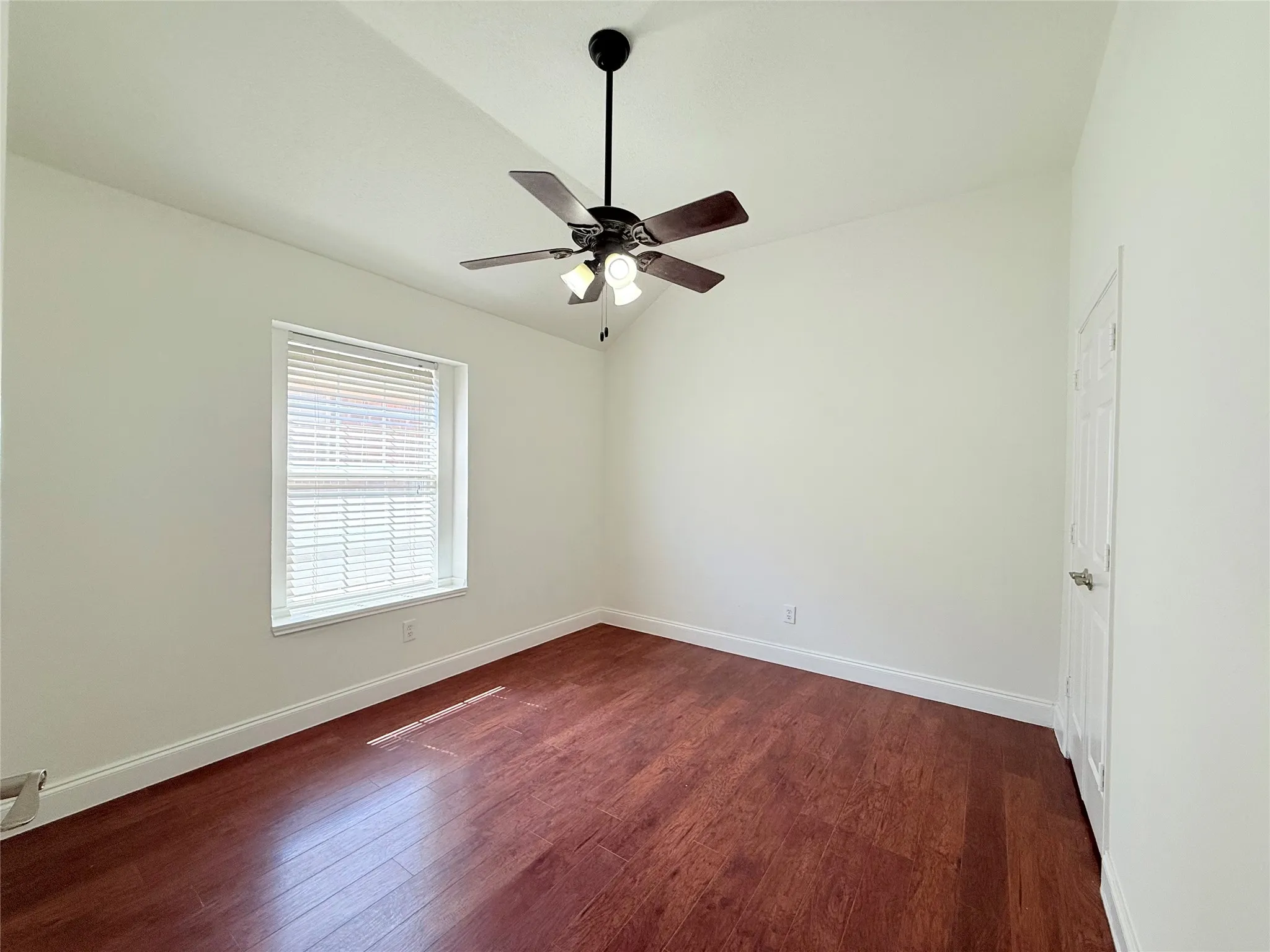 Vaulted ceiling with a ceiling fan light fixture, wood-finish flooring, and a single window with blinds
