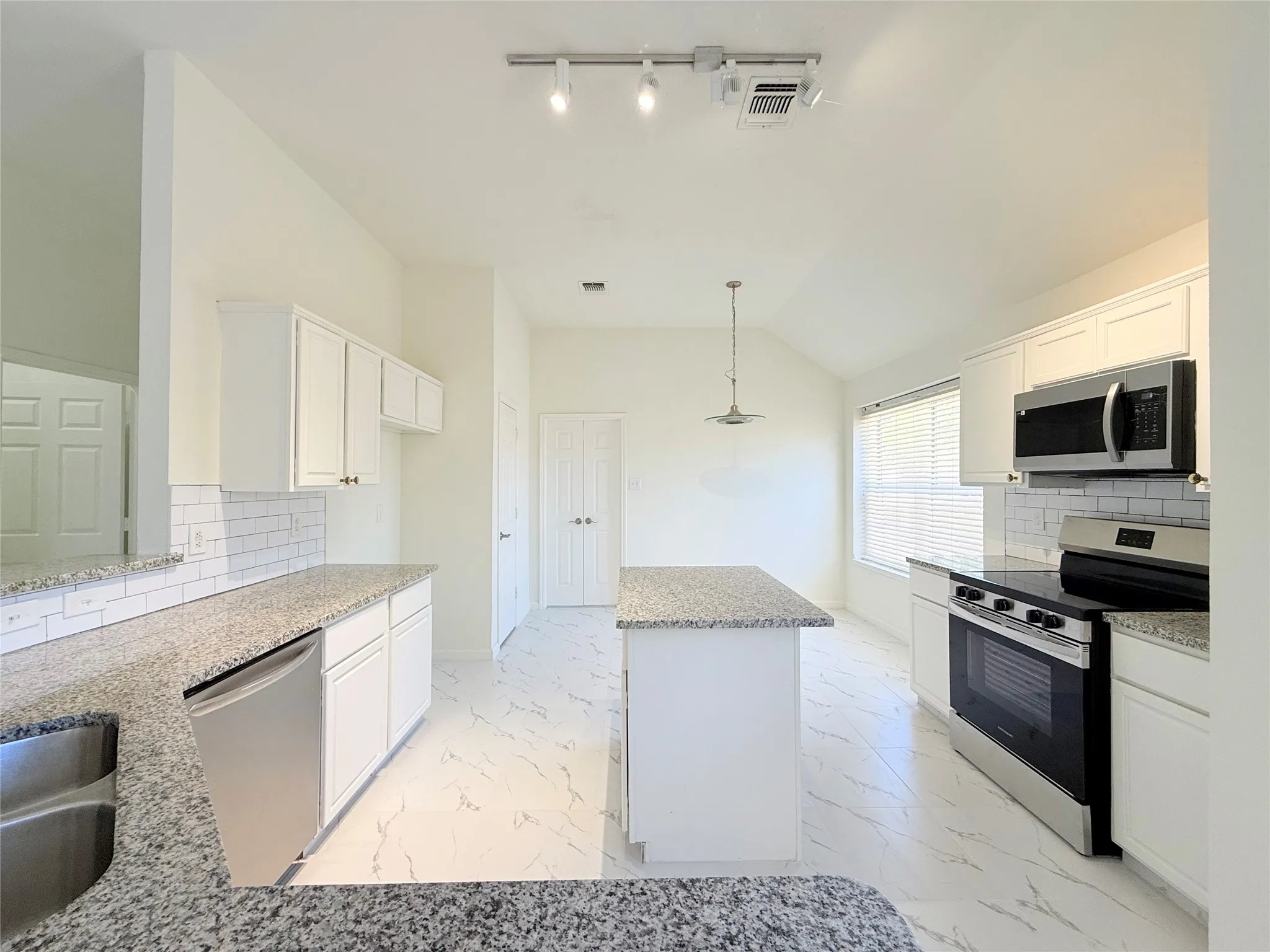 Kitchen featuring white cabinetry, granite countertops, stainless steel appliances, a subway tile backsplash, and a central island