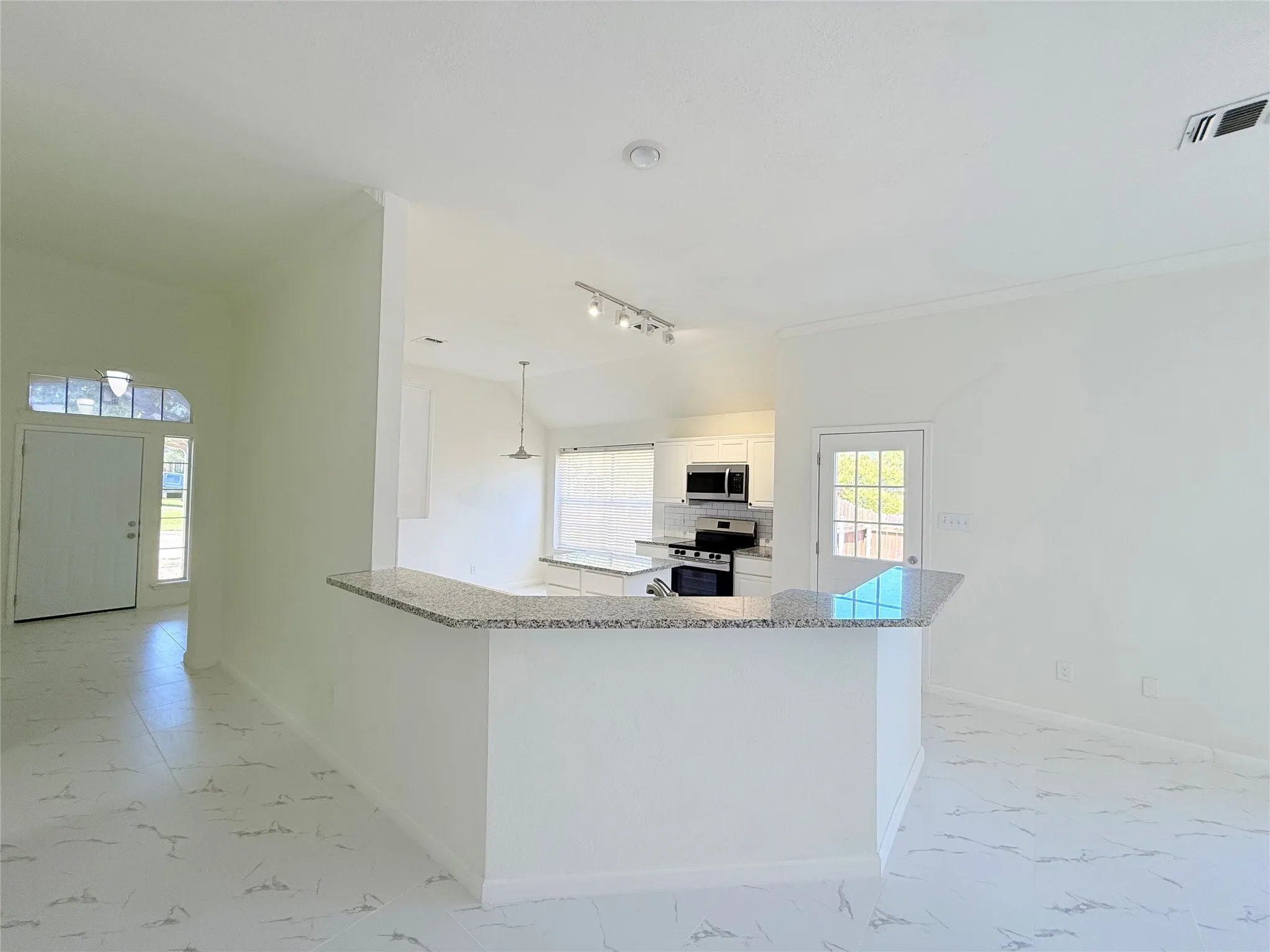 White tile flooring, kitchen island with granite countertop, stainless steel appliances, track lighting, and a front entry door with an arched transom