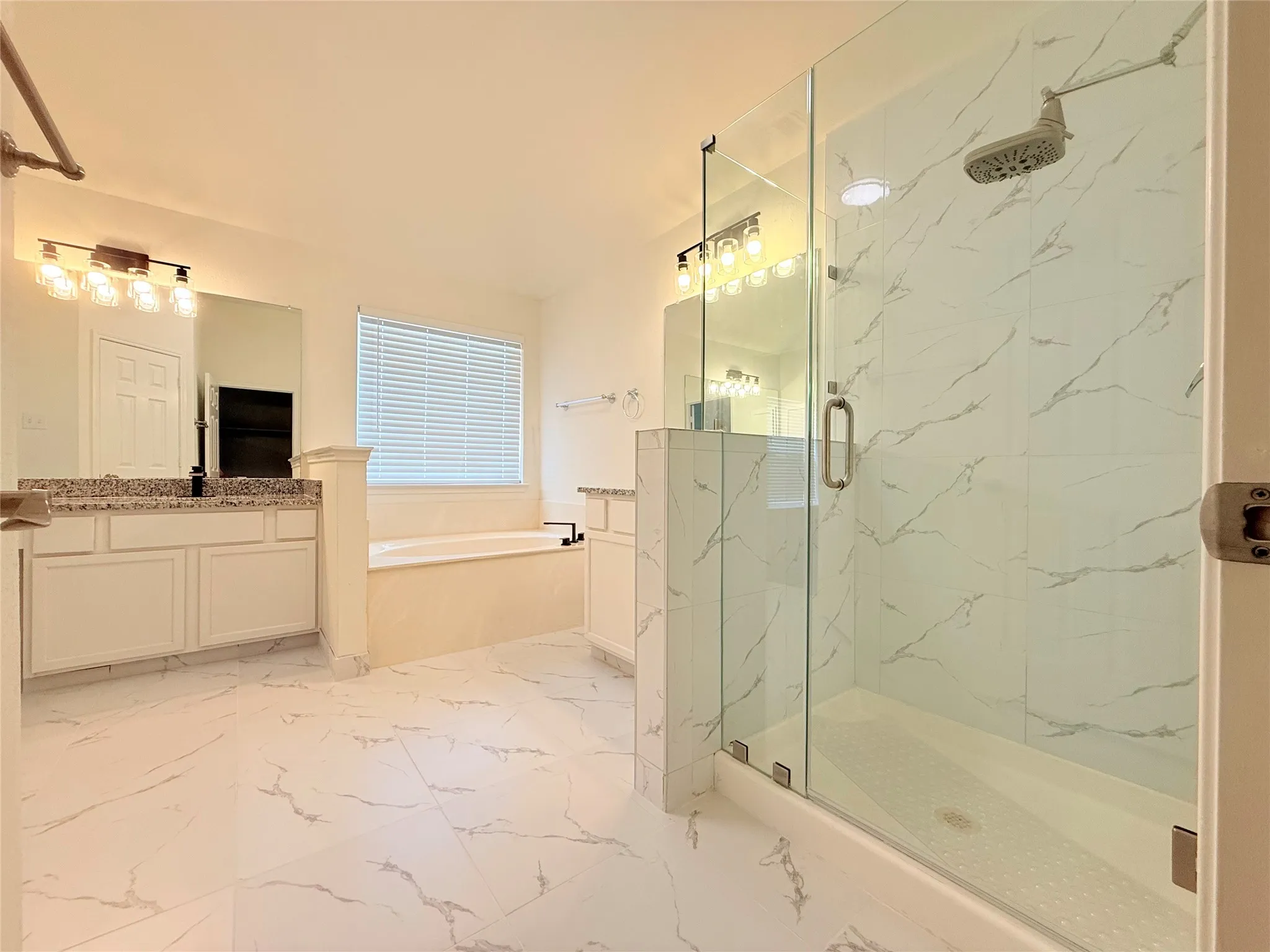 Spacious bathroom featuring a glass-enclosed shower, a separate soaking tub, and dual vanities with granite countertops