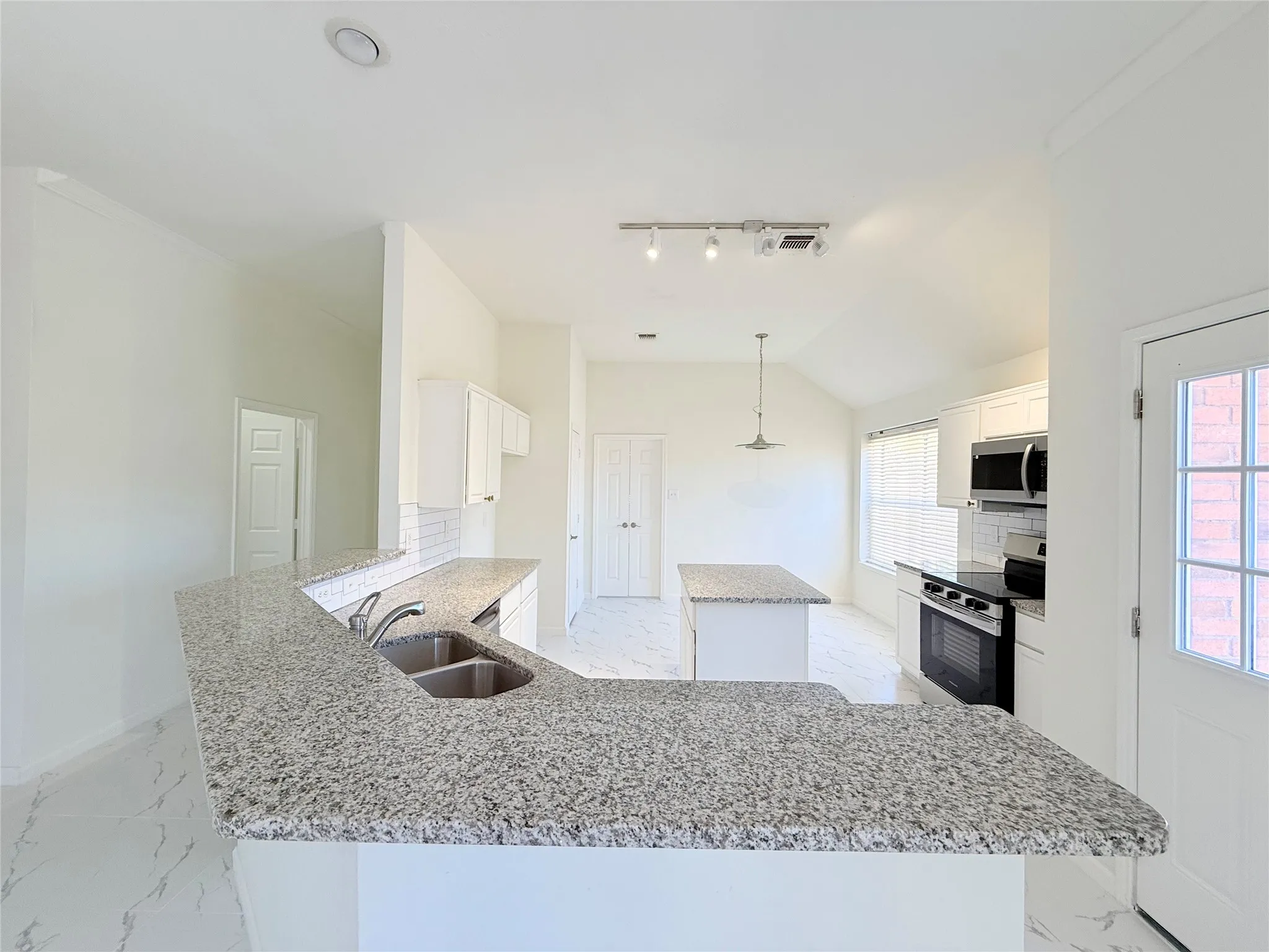 Kitchen featuring granite countertops, stainless steel appliances, white cabinetry, a kitchen island, and a dual basin sink