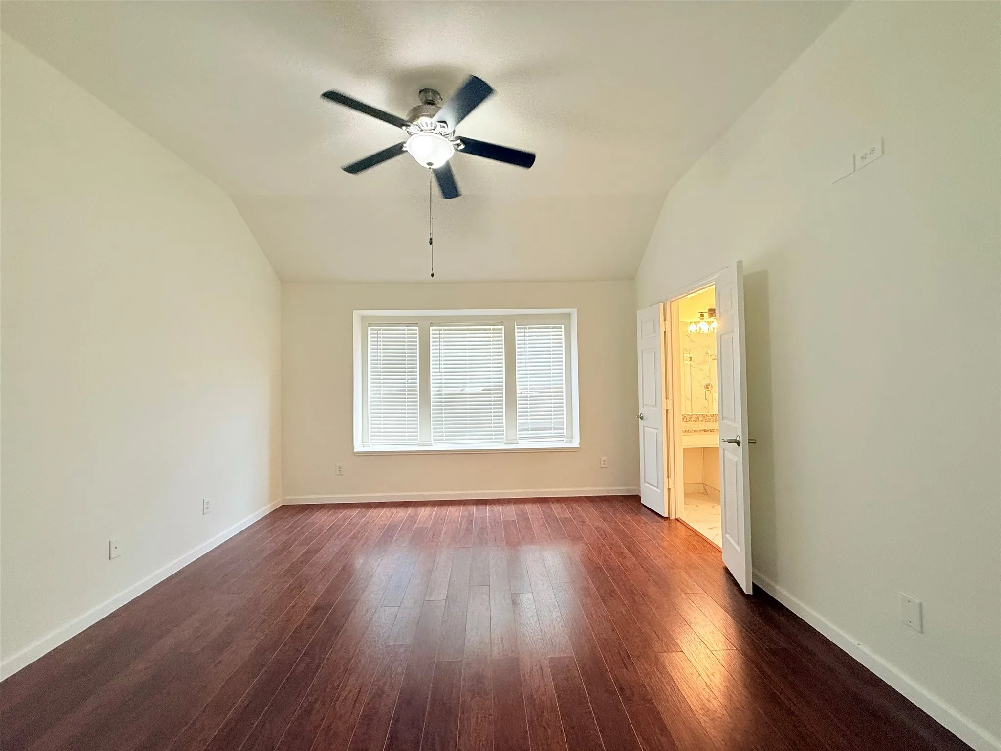 Vaulted ceiling with a ceiling fan, bay window with blinds, wood-finish flooring, and double doors to an adjacent bathroom
