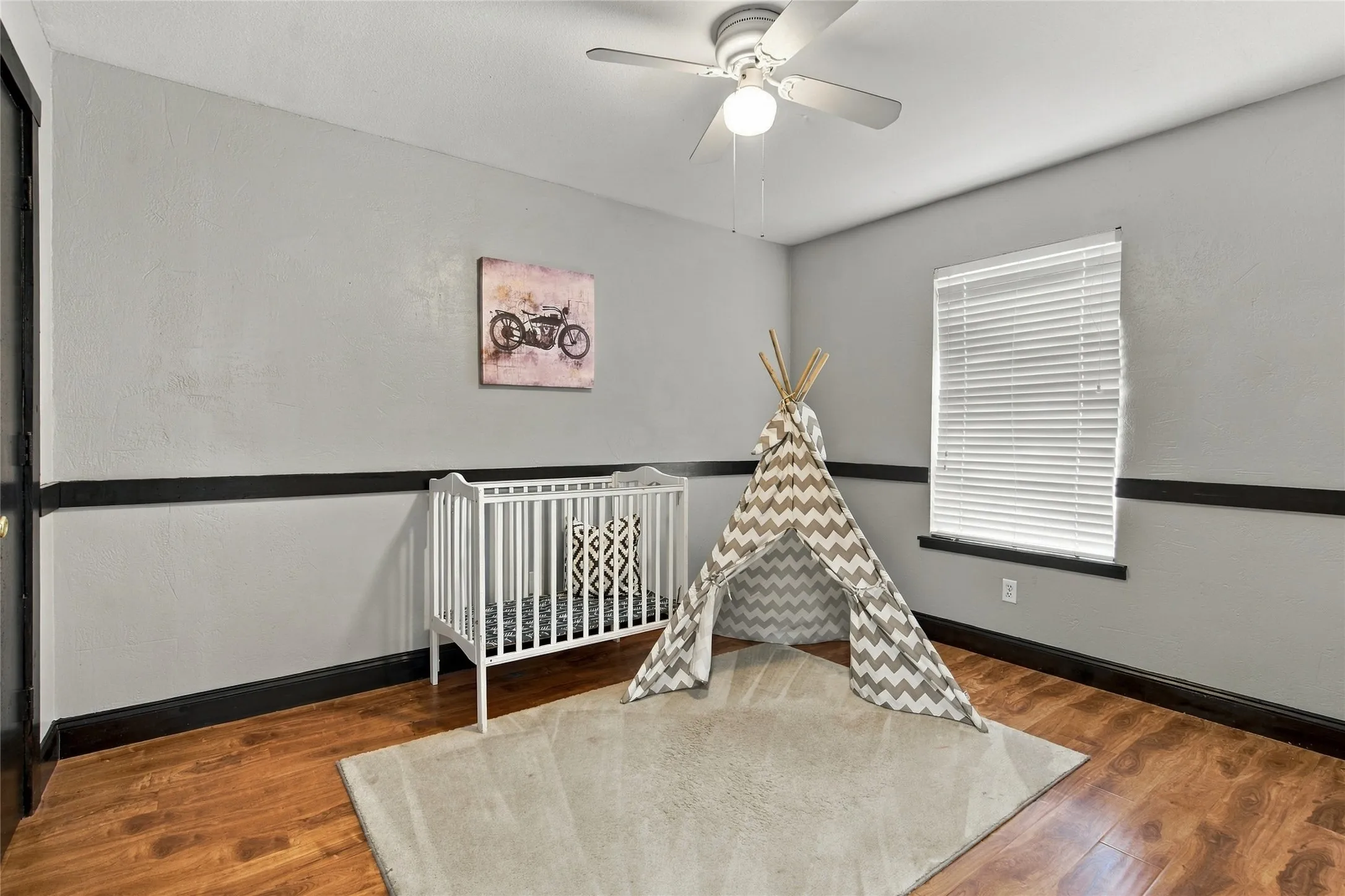 Wood-finish flooring, single window with blinds, ceiling fan, and a painted chair rail accent