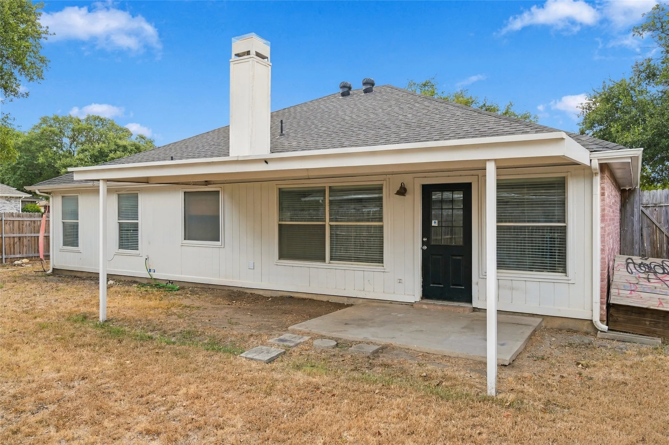 Clean-lined ranch home featuring a covered front porch, expansive windows with horizontal blinds, a tall brick chimney, and a gently sloped asphalt shingle roof