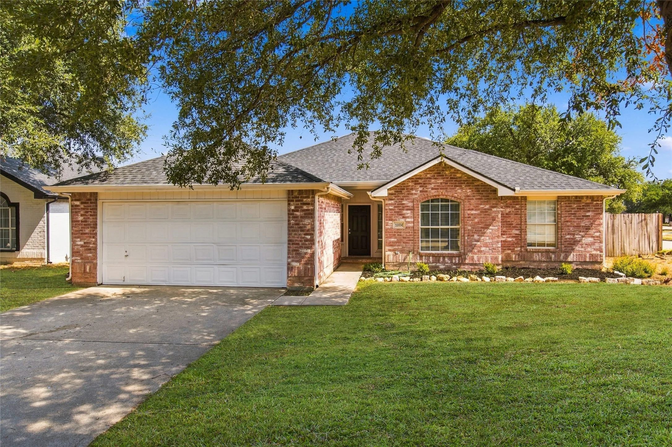 Red brick exterior with a gray shingle roof, arched window, and attached two-car garage