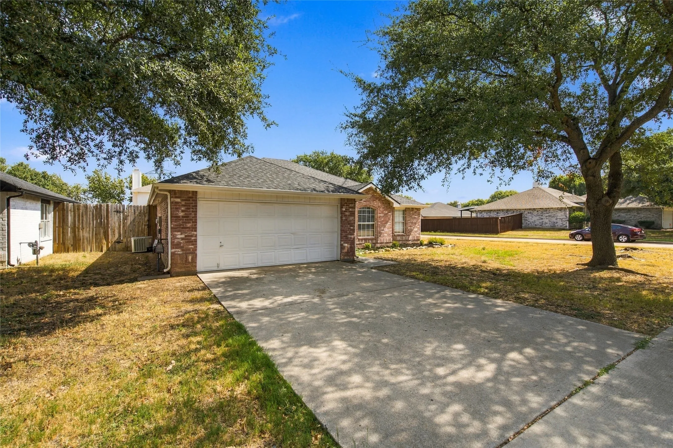 Brick facade home with an attached two-car garage, concrete driveway, and mature trees