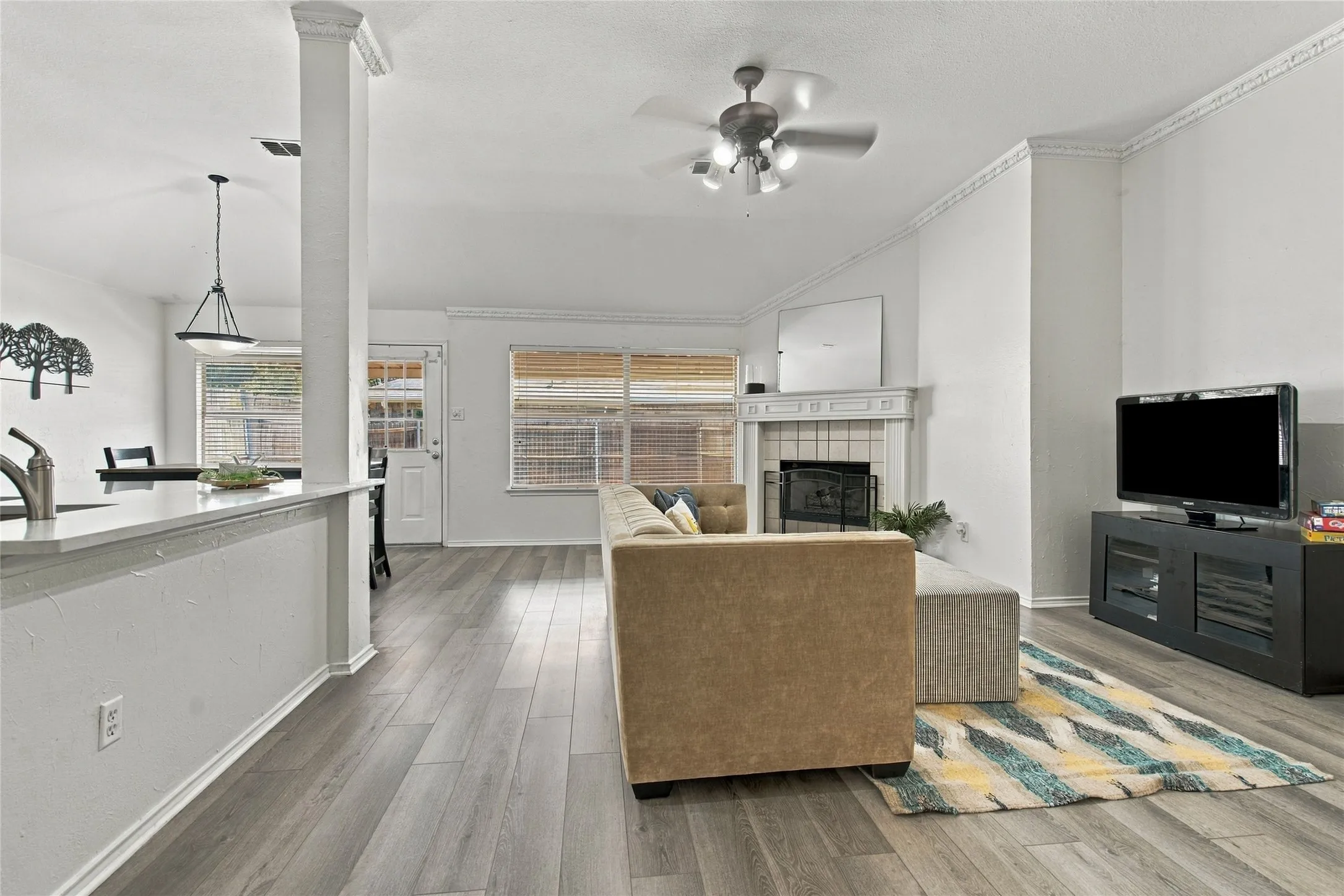 Vaulted ceiling with a ceiling fan, fireplace with a tile surround, wood-finish flooring, and crown molding